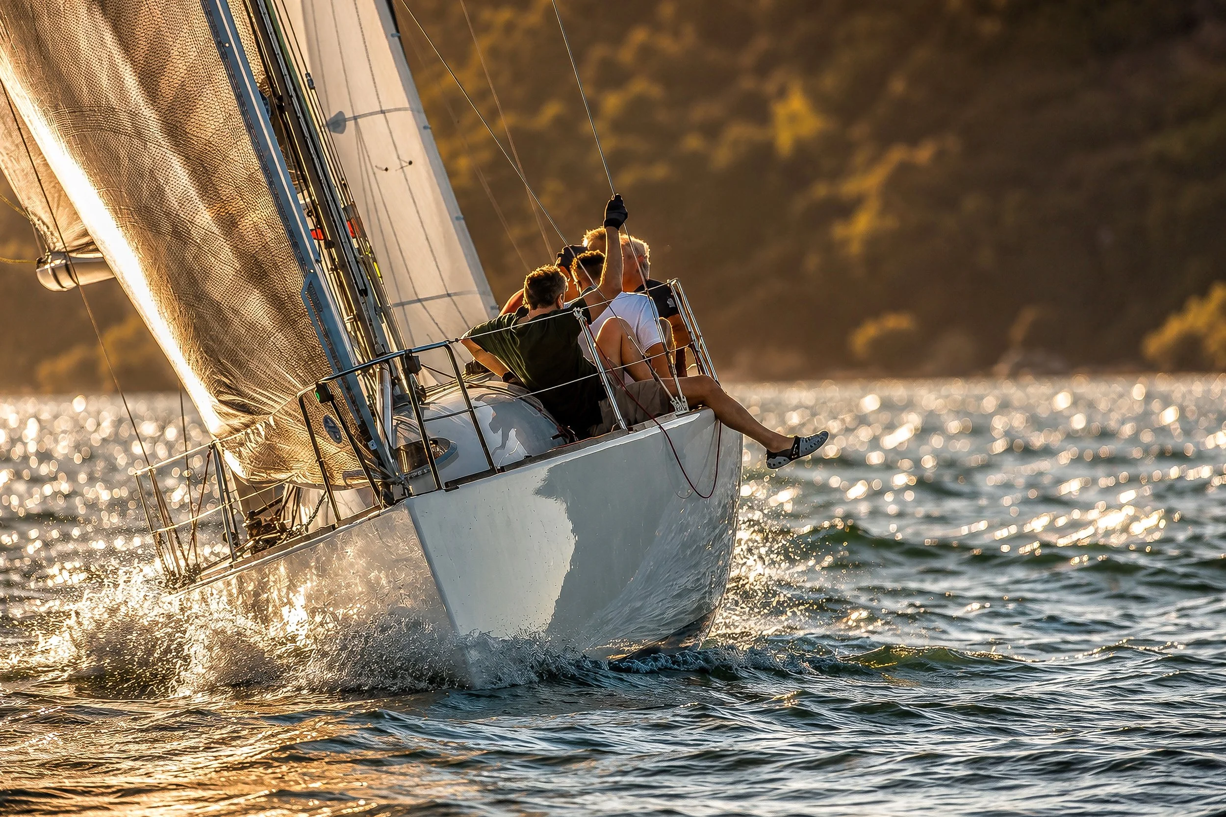 A group of people sailing a boat on the water during sunset, with the sun casting a golden glow and the water shimmering.