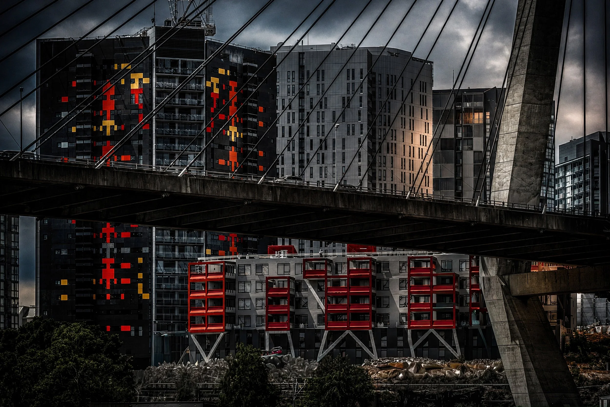 A dramatic night photograph of Anzac Bridge featuring illuminated office windows, reflections and strong geometric lines beneath a moody sky.
