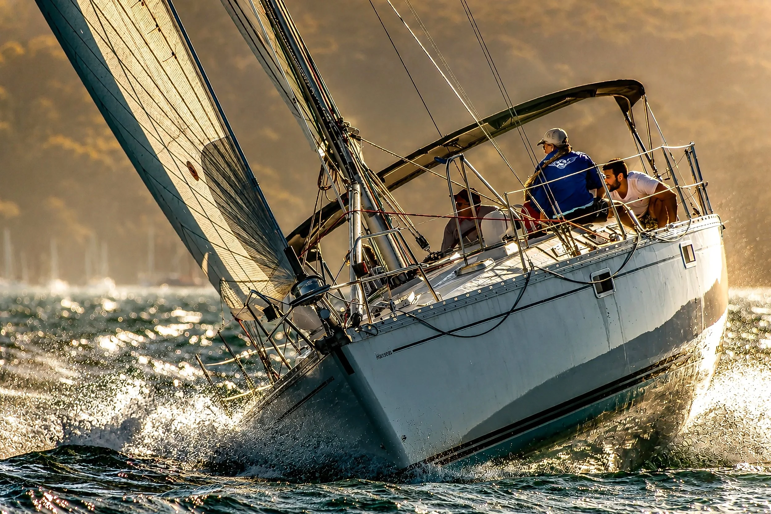 Sailboat cutting through water at sunset with crew members on deck.