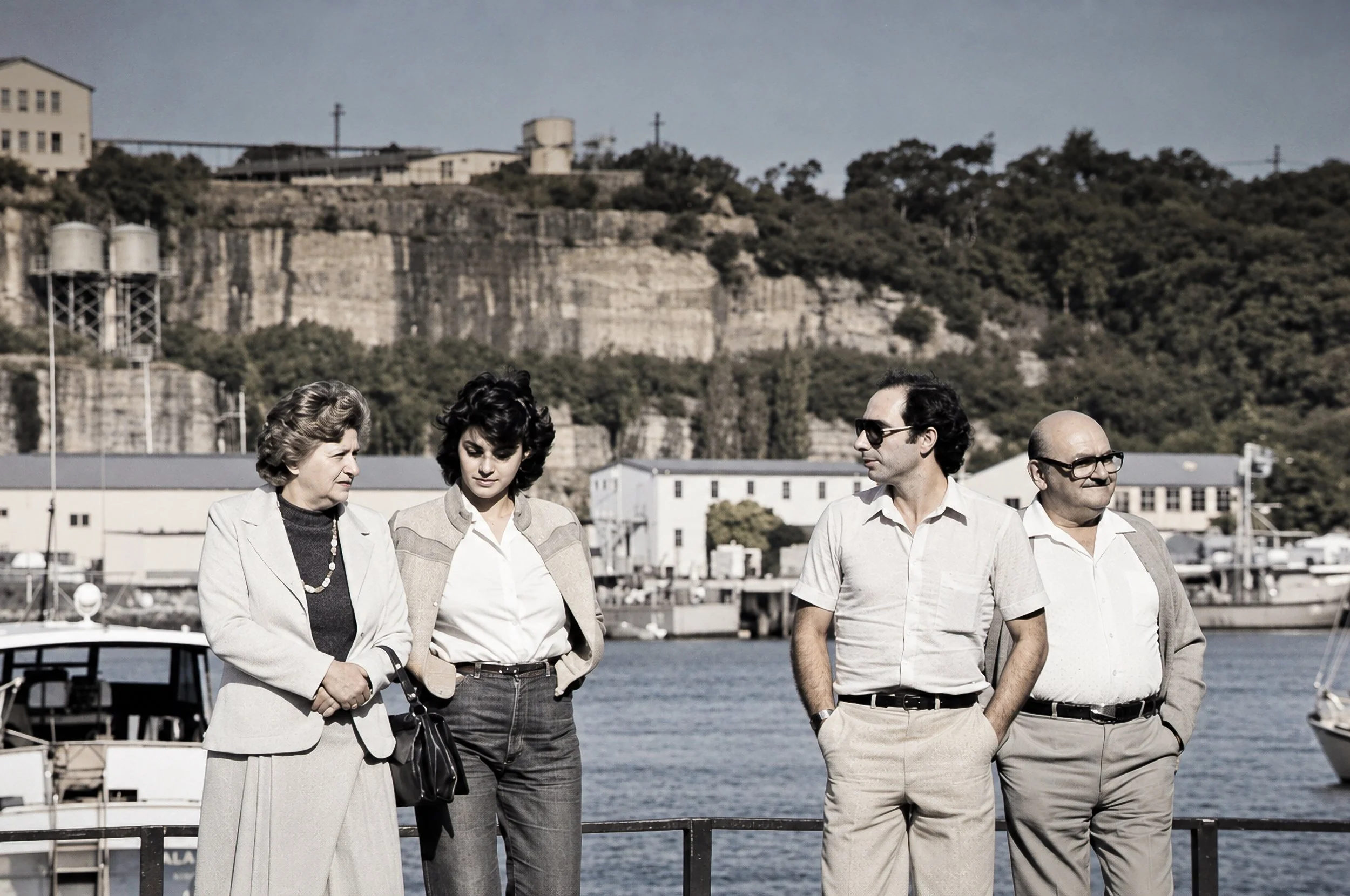 People Beside Sydney Harbour - Four people pause together beside the harbour, surrounded by boats, waterfront buildings and the movement of Sydney beyond them. The relaxed interaction gives the photograph an intimate documentary quality.