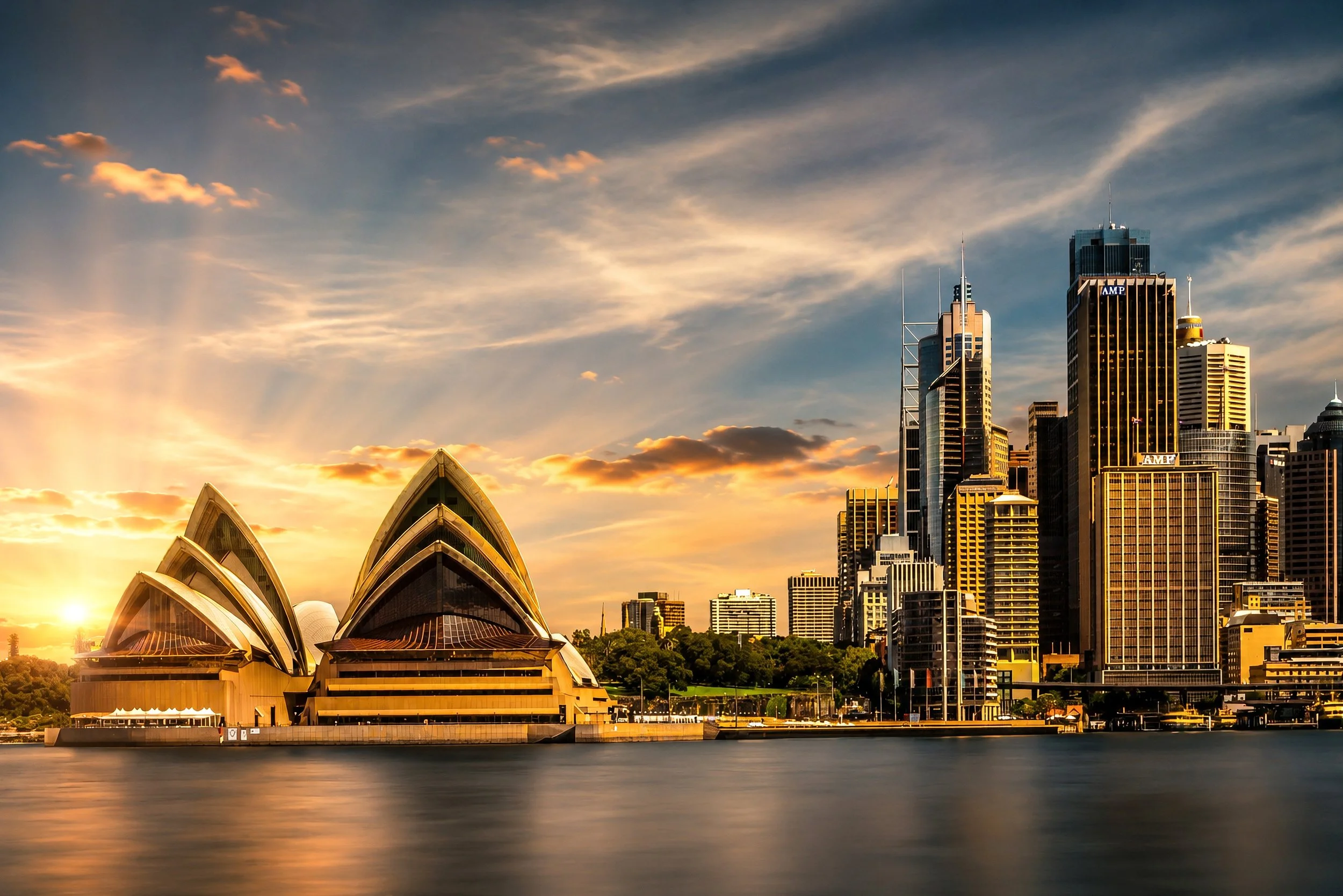 The Sydney Opera House and city skyline glow beneath golden sunrise clouds across Sydney Harbour in this fine art cityscape.
