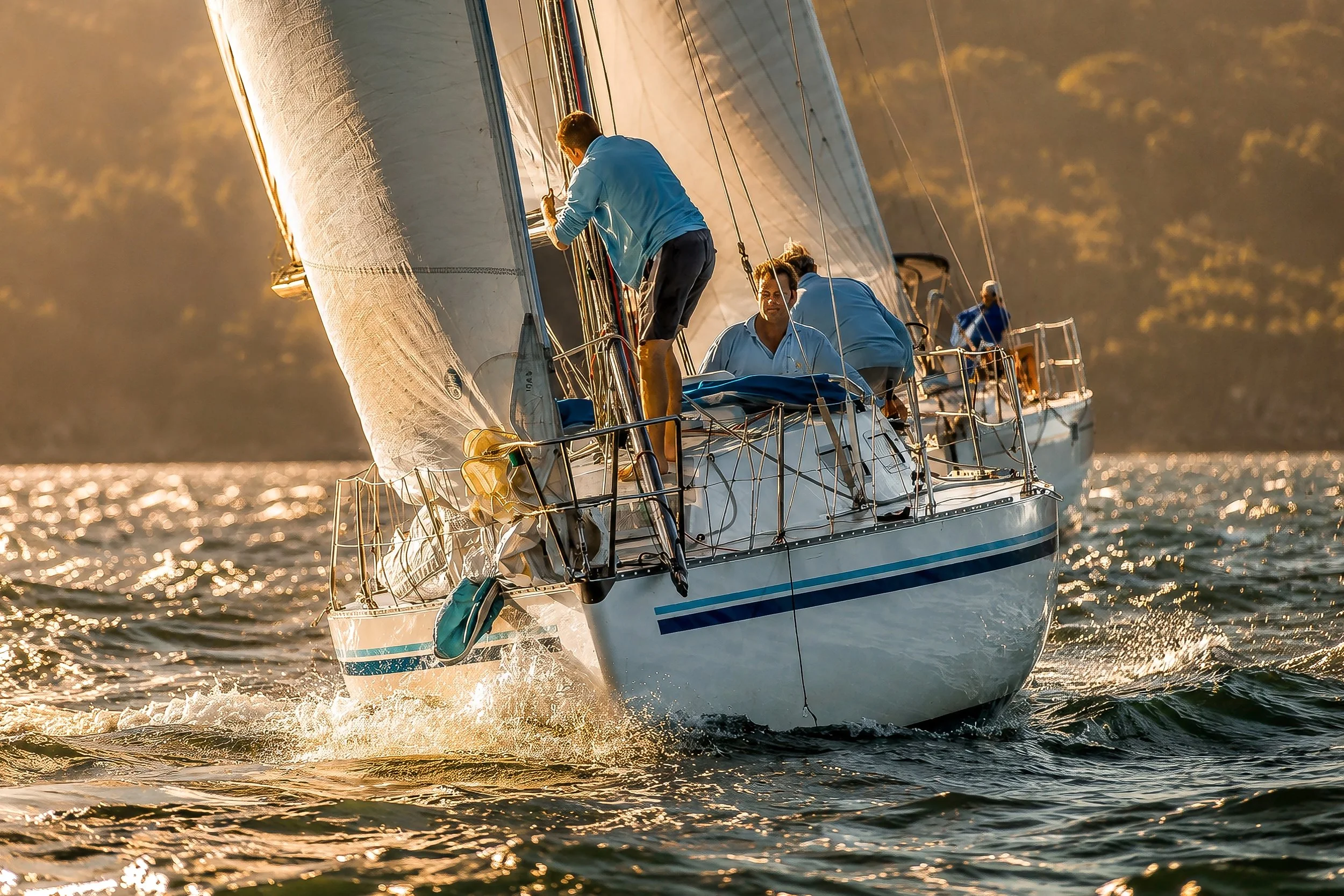 People sailing on a boat during sunset or sunrise, with sunlight reflecting off the water.