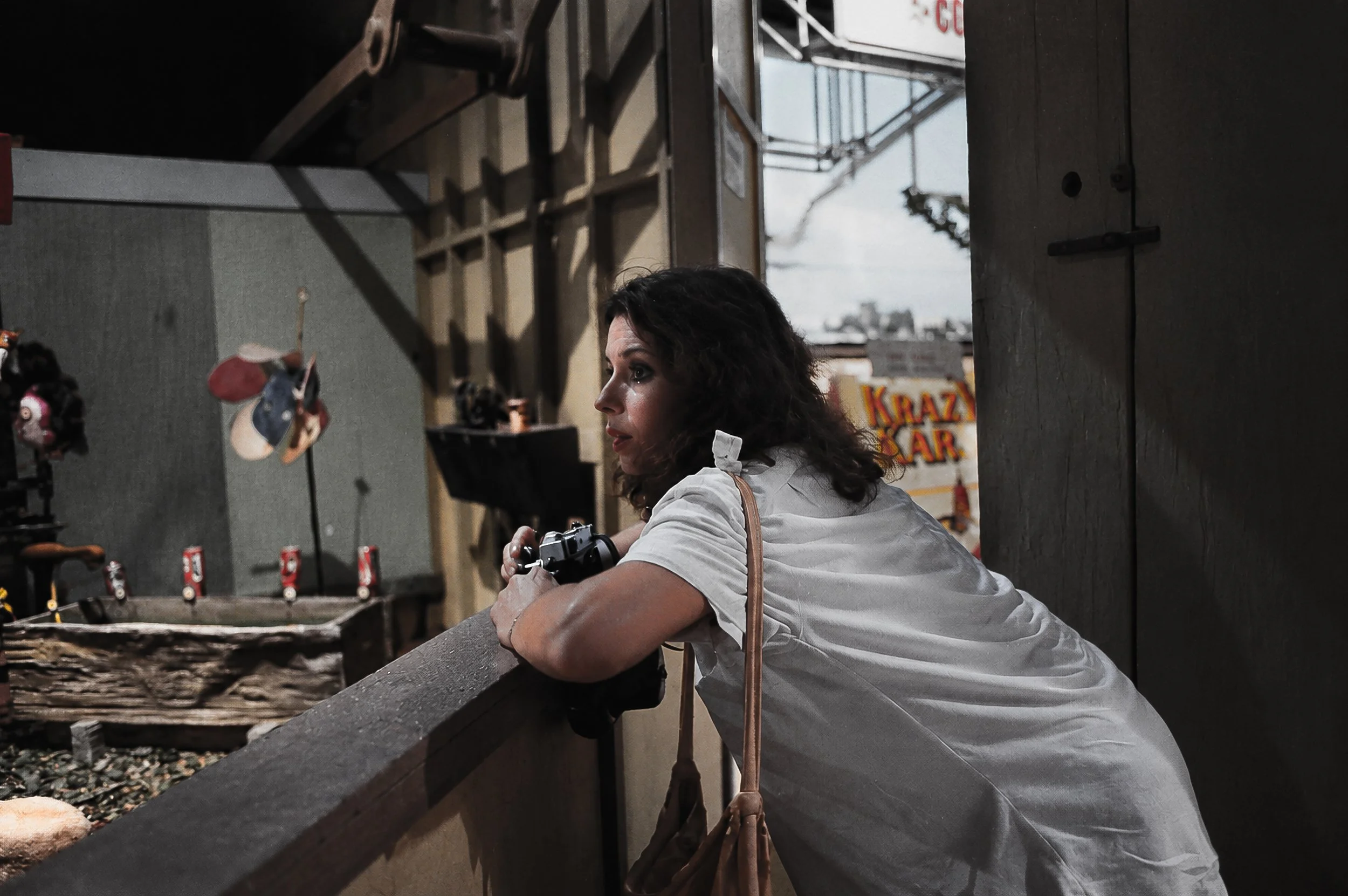 Woman with Camera - A woman leans over a railing holding a camera, absorbed in the activity beyond her. The intimate composition introduces another photographer into the story and creates a quiet moment within the busy urban environment.
