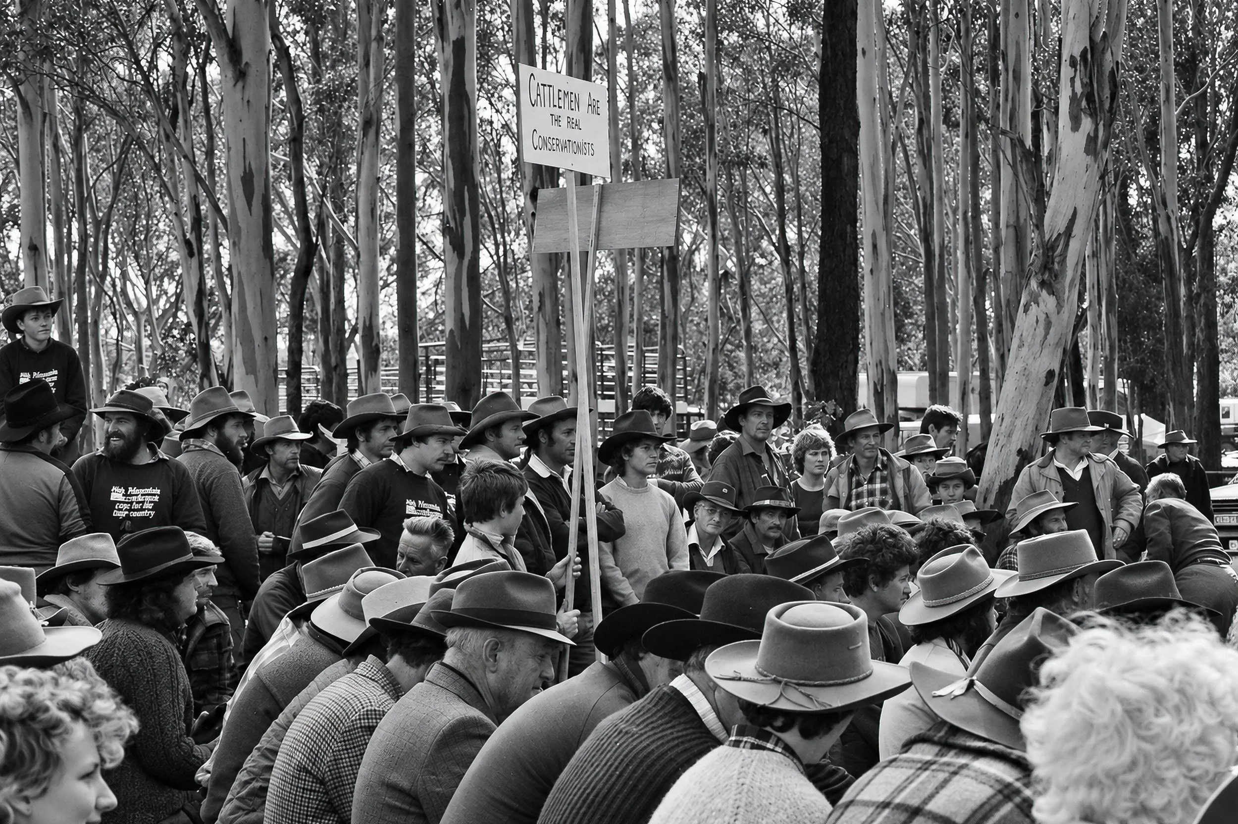 Cattlemen and Supporters - Hundreds of people gather beneath the trees, surrounded by the distinctive hats and clothing of the High Country cattlemen. A protest sign rises above the crowd, expressing the cattlemen's view of their role as custodians o