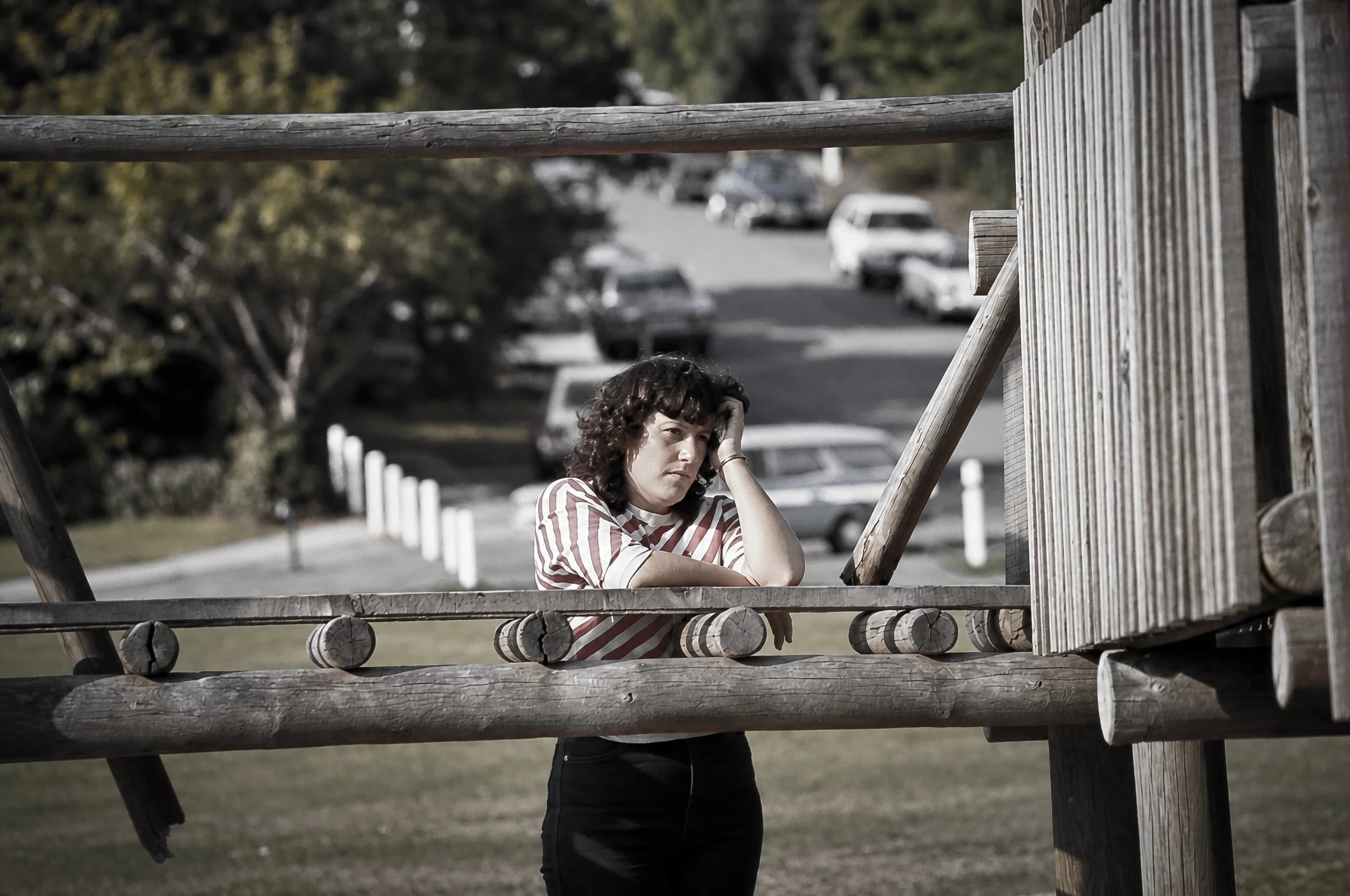 Woman Behind the Railing - A woman pauses behind a wooden railing, framed by the surrounding architecture and the street beyond. The photograph transforms an ordinary moment into a quiet study of people and place.