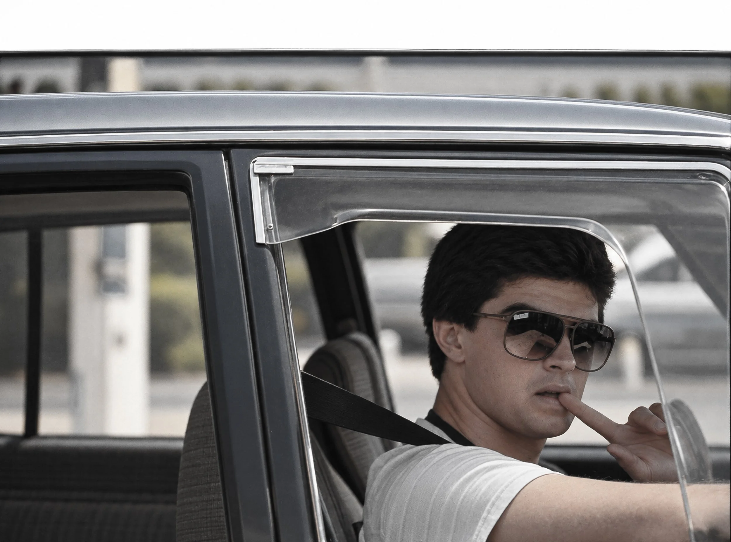 Driver with Sunglasses - A young driver glances across from behind the wheel, sunglasses and cigarette adding unmistakable character to this candid Sydney street encounter. The car window and interior frame the subject, preserving the spontaneous atm