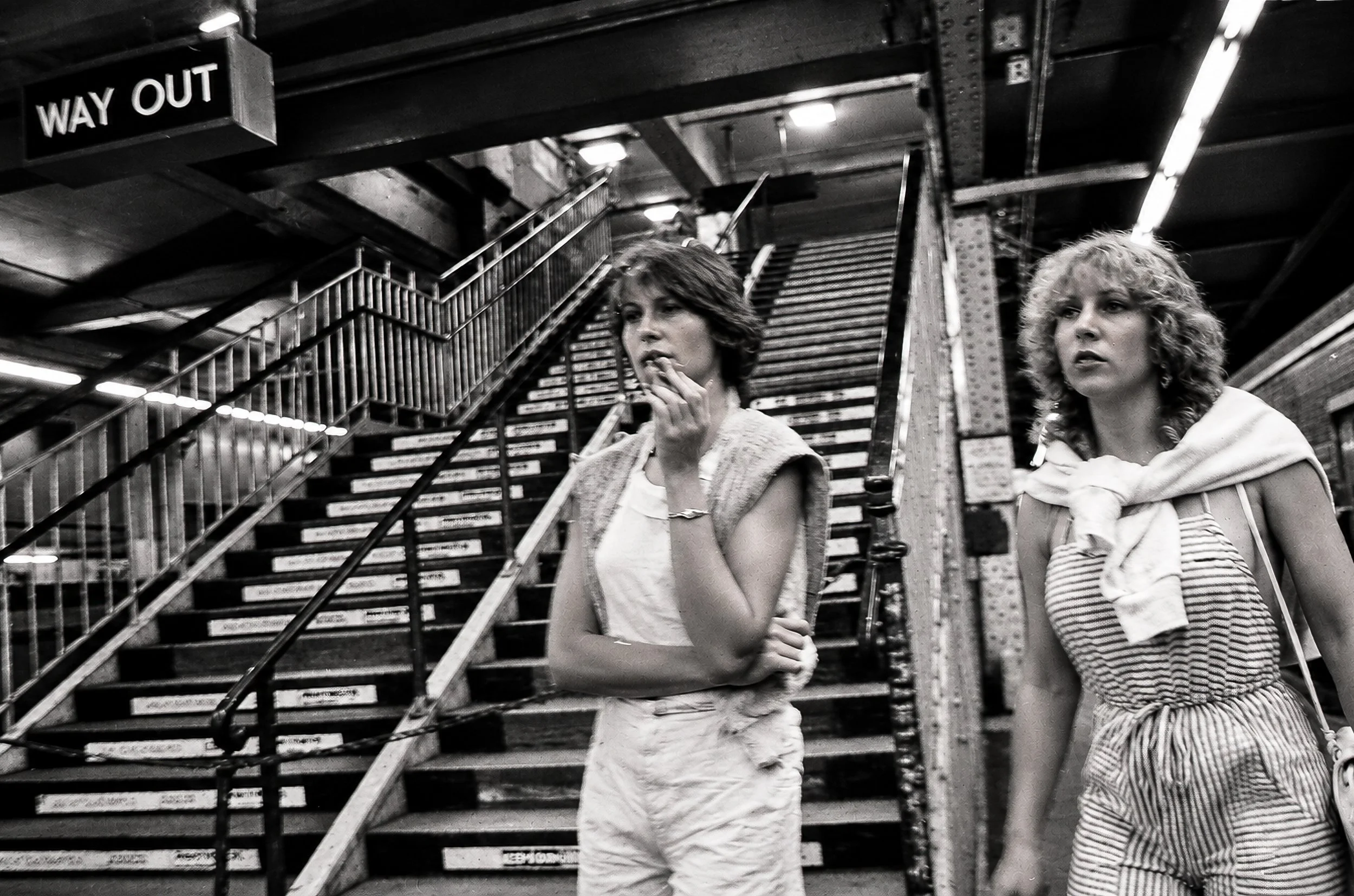 Coming Up the Stairs - Two women walk toward the camera beside the station stairway. Their clothing, expressions and the surrounding railway architecture give the photograph an unmistakably candid, everyday quality.
