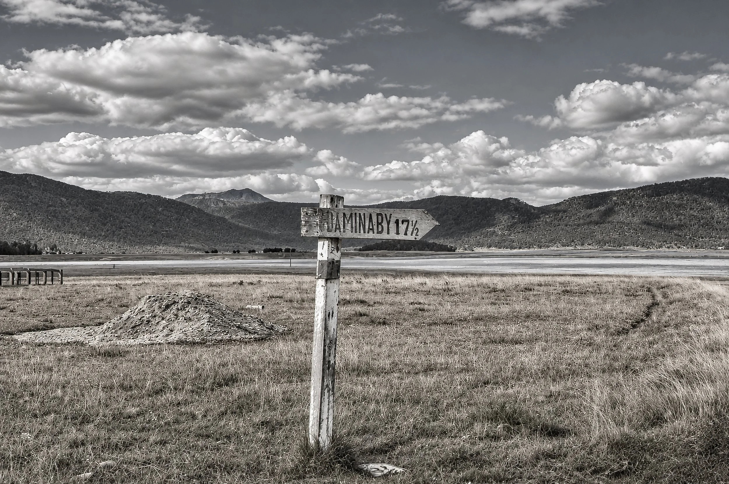 Adaminaby 17 Miles - A roadside sign marks the distance to Adaminaby, standing alone against the broad landscape of the Snowy Mountains. The simple sign becomes a reminder of the distances covered on a journey made largely on horseback.