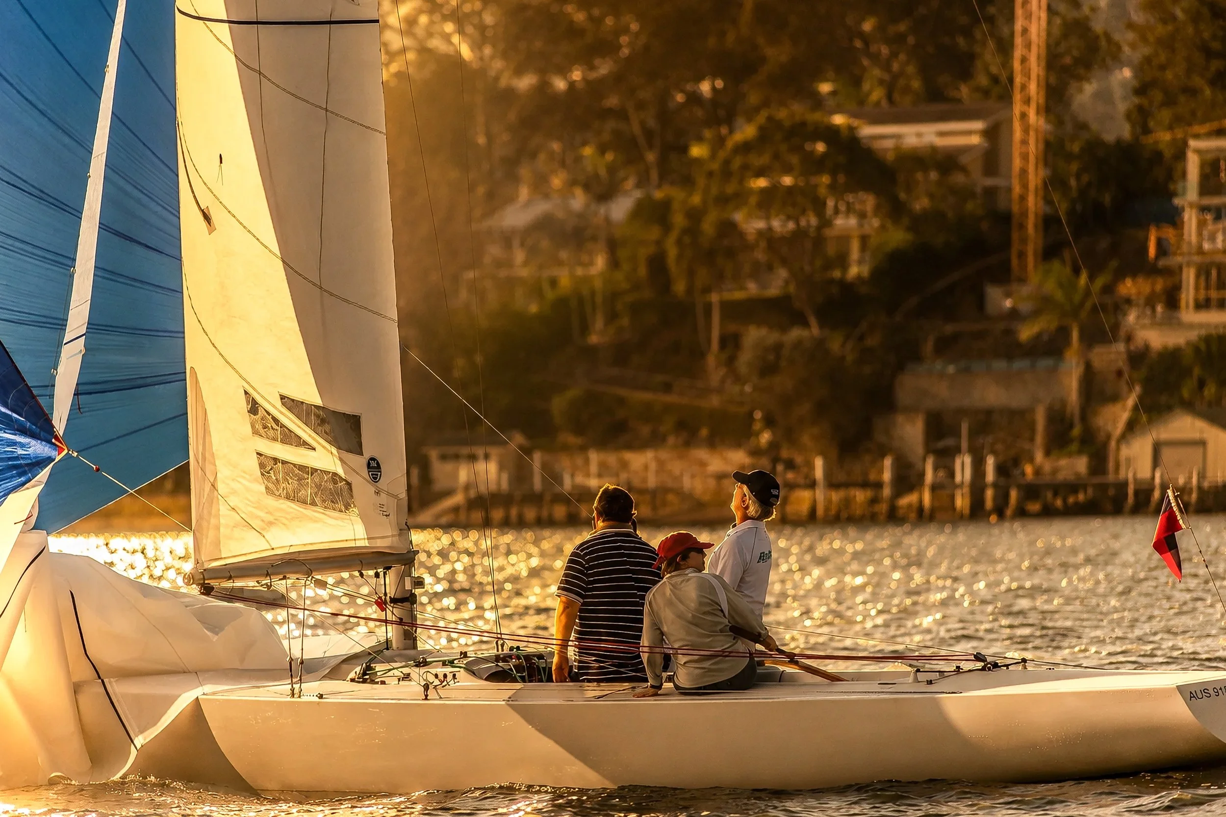 People sailing on a boat during sunset with a cityscape and trees in the background.
