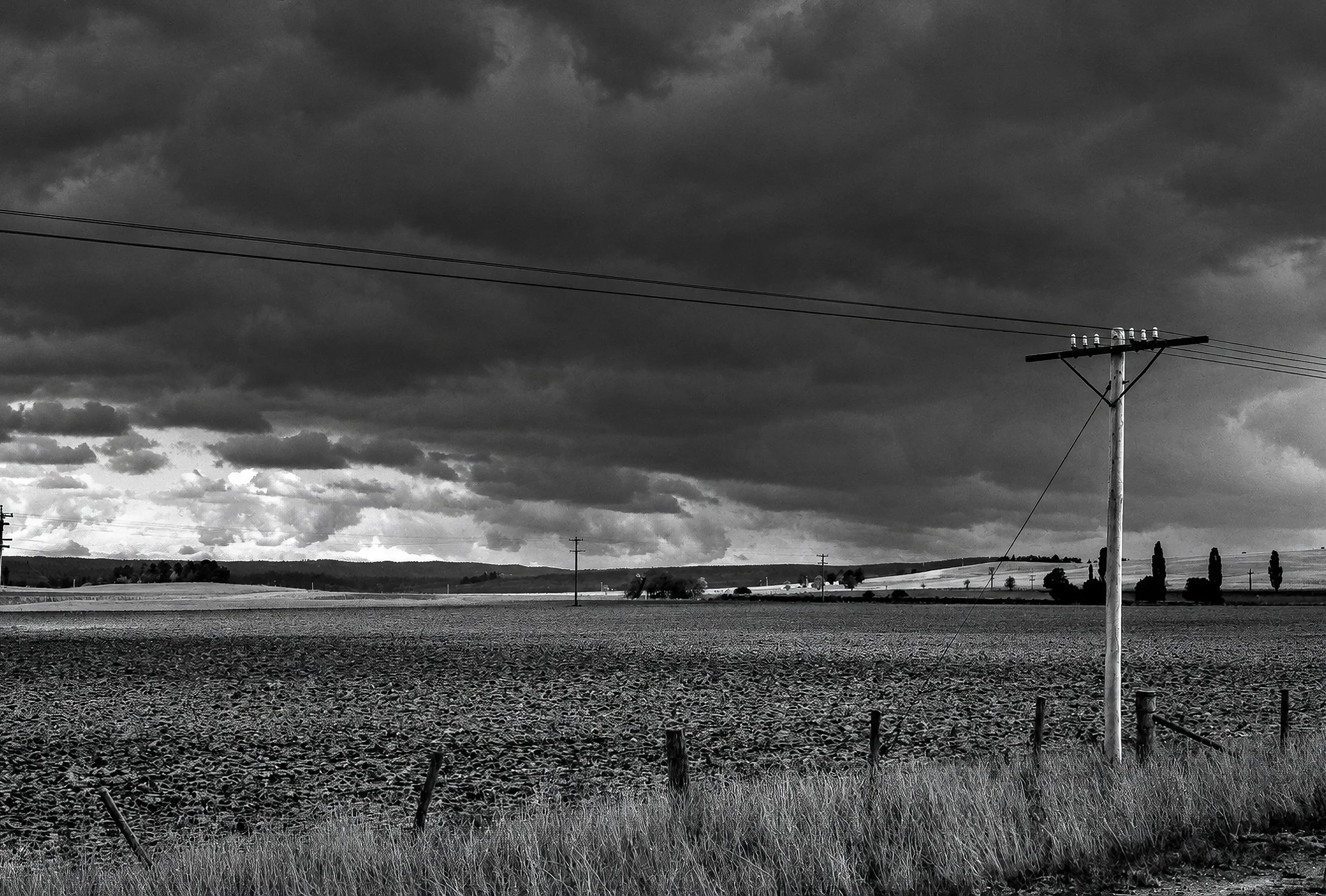 The Open Country - An isolated power pole stands beside the open fields beneath a huge, changing sky. The simplicity of the composition — field, horizon, pole and cloud — captures the character of the plains encountered during the journey towards the