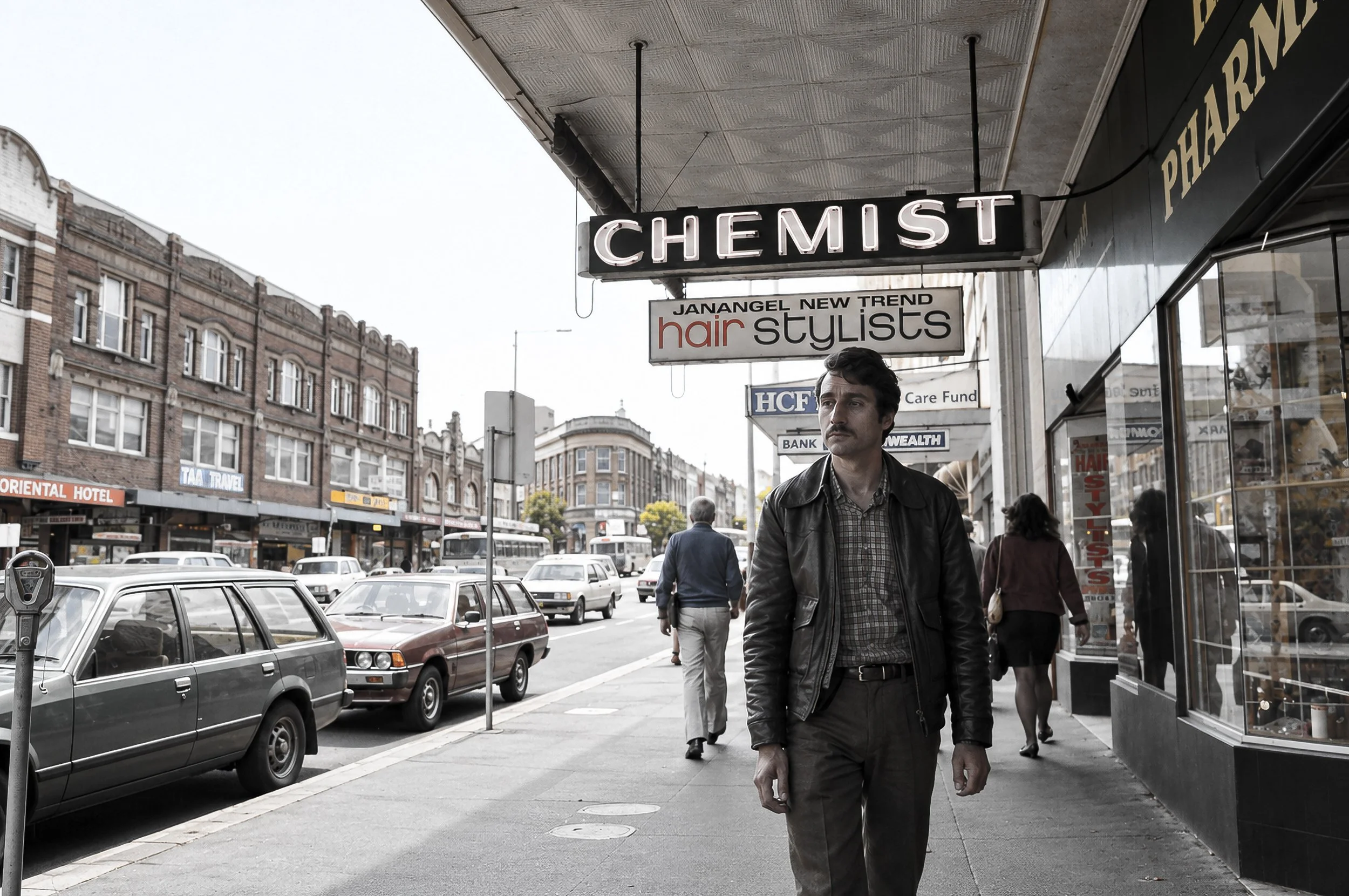 Sydney Street - CHEMIST - A man walks beneath the prominent CHEMIST sign while traffic and pedestrians move through the surrounding city street. Period vehicles, shopfronts and signage add to the photograph's documentary record of Sydney.