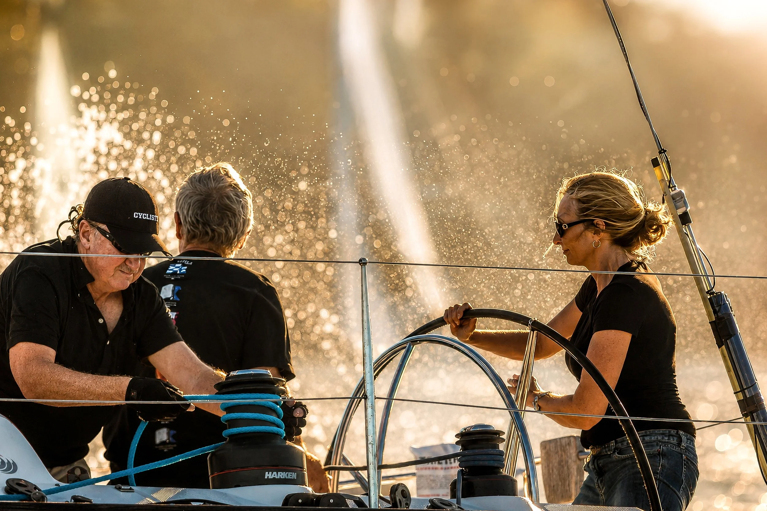 Four people are on a boat, working together, with water droplets and sunlight in the background.