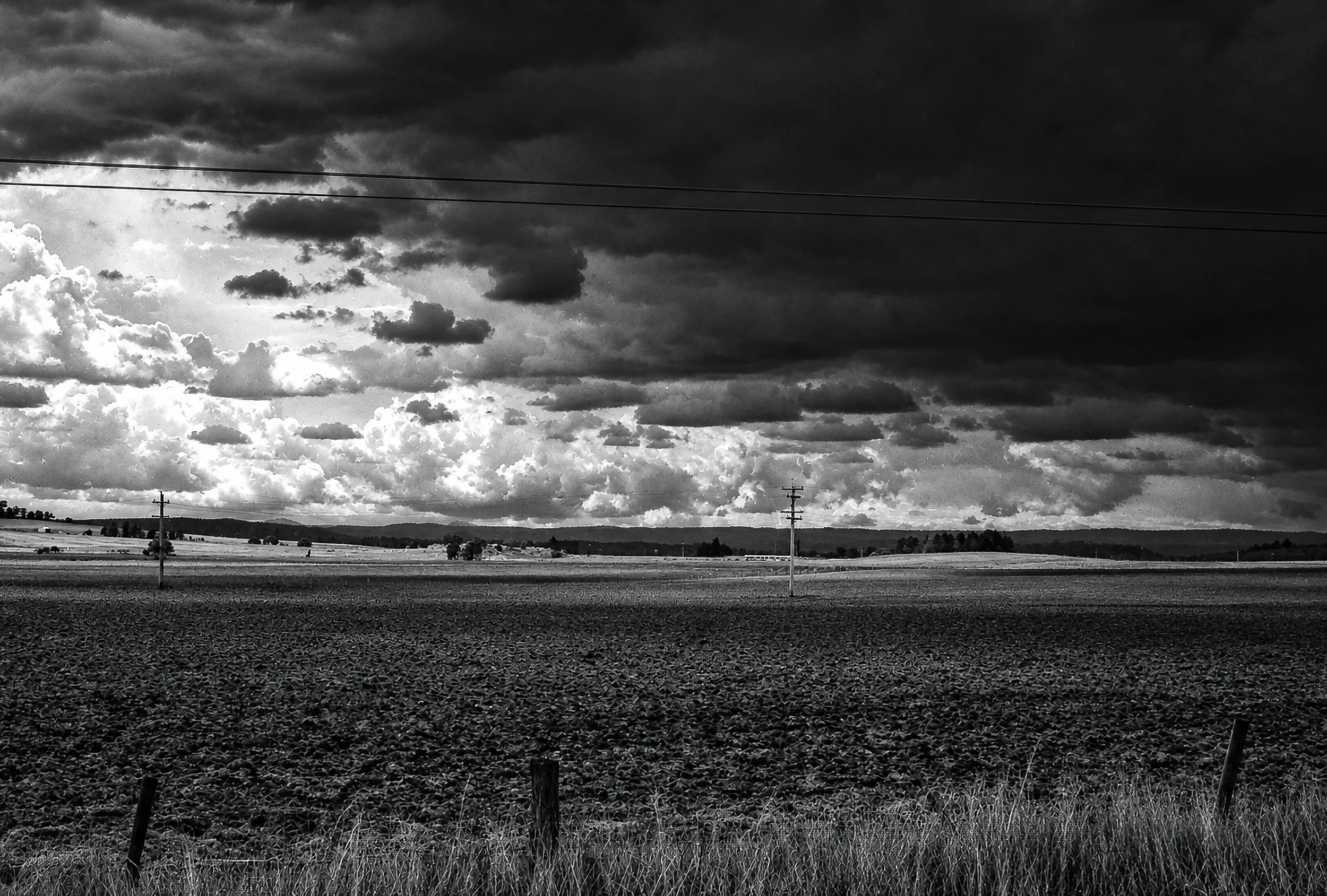 Storm Over the Plains - A broad agricultural landscape lies beneath an immense and threatening sky. Bright breaks in the clouds contrast sharply with the approaching darkness, while the open fields and distant horizon emphasise the extraordinary scal