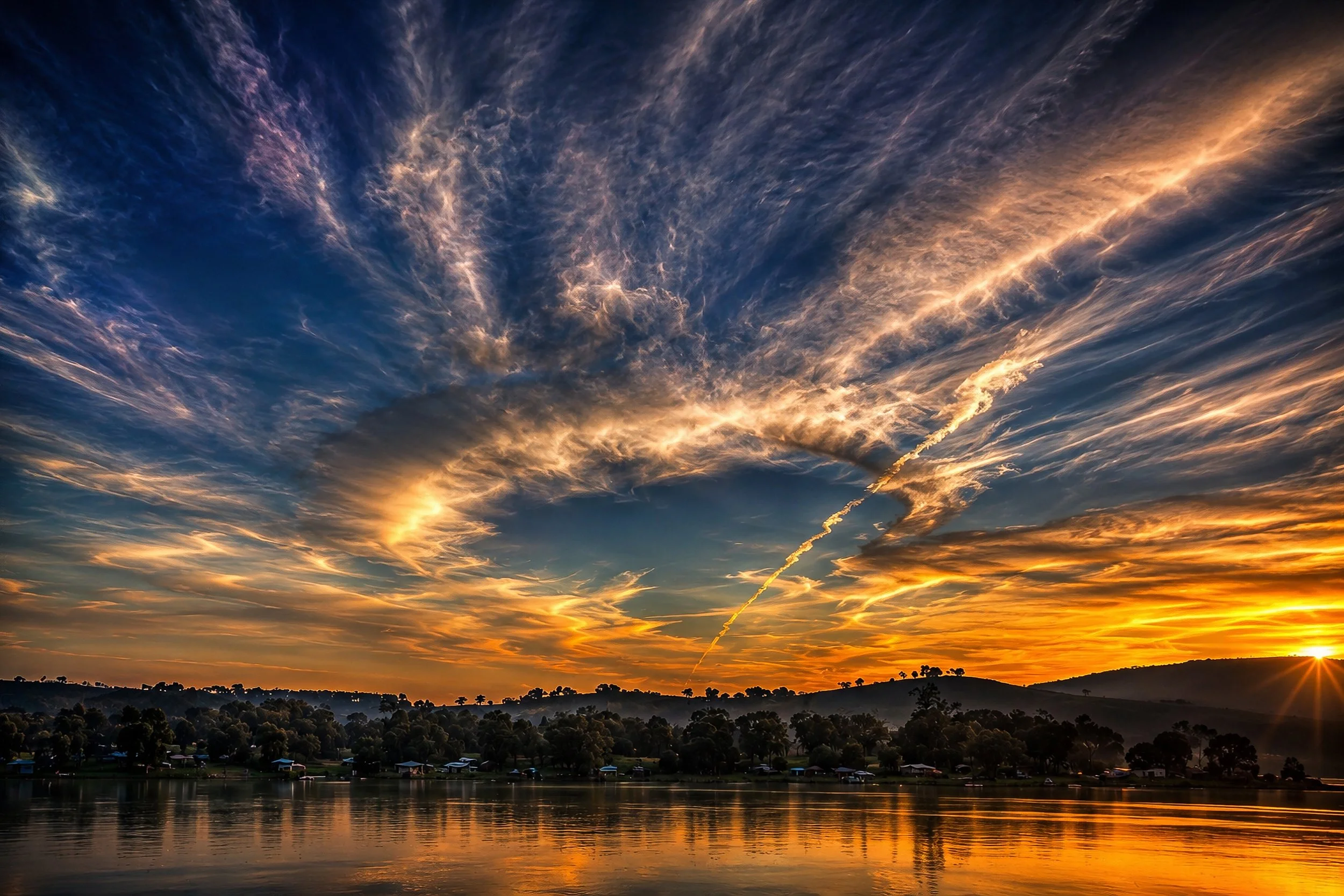 A spectacular Australian sunrise fills the sky with sweeping orange and blue cloud formations reflected across calm water.
