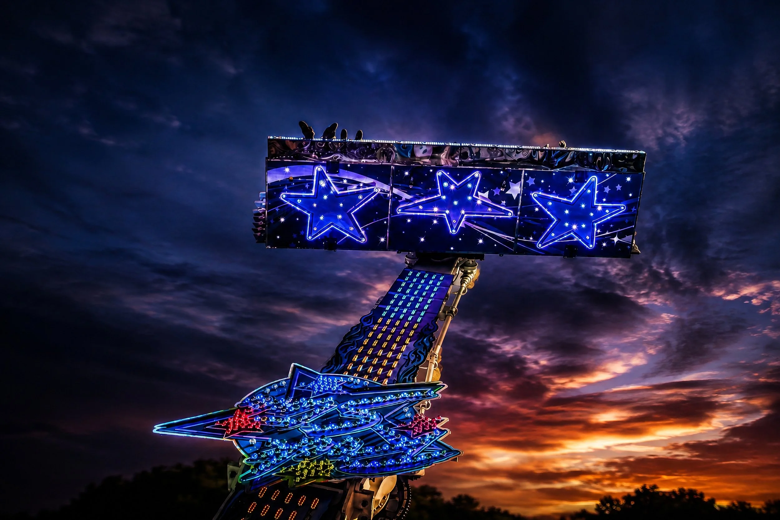 An illuminated carnival ride decorated with glowing blue stars photographed against a dramatic night sky.