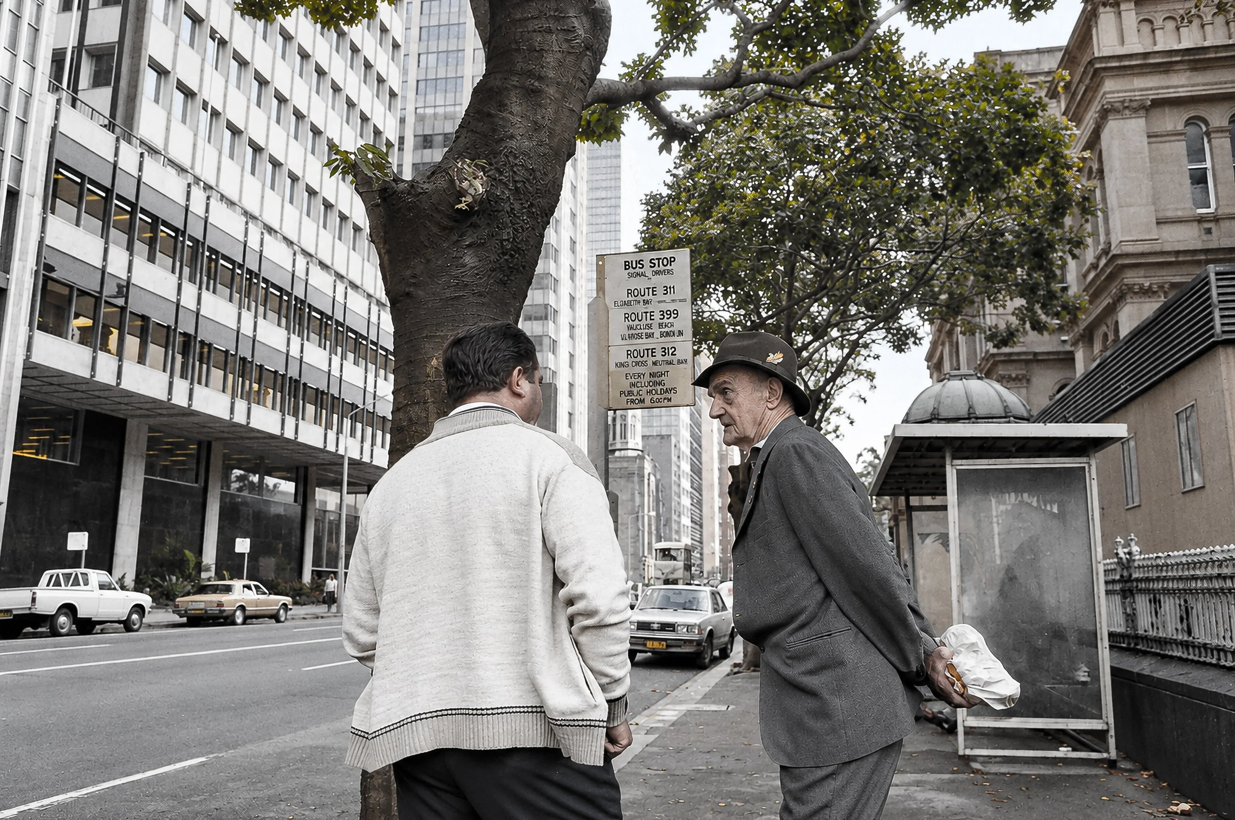 Two Men Talking in Sydney - Two men pause in conversation on a Sydney street, surrounded by the architecture and activity of the city. Their informal interaction provides a simple, intimate moment within the larger urban environment.