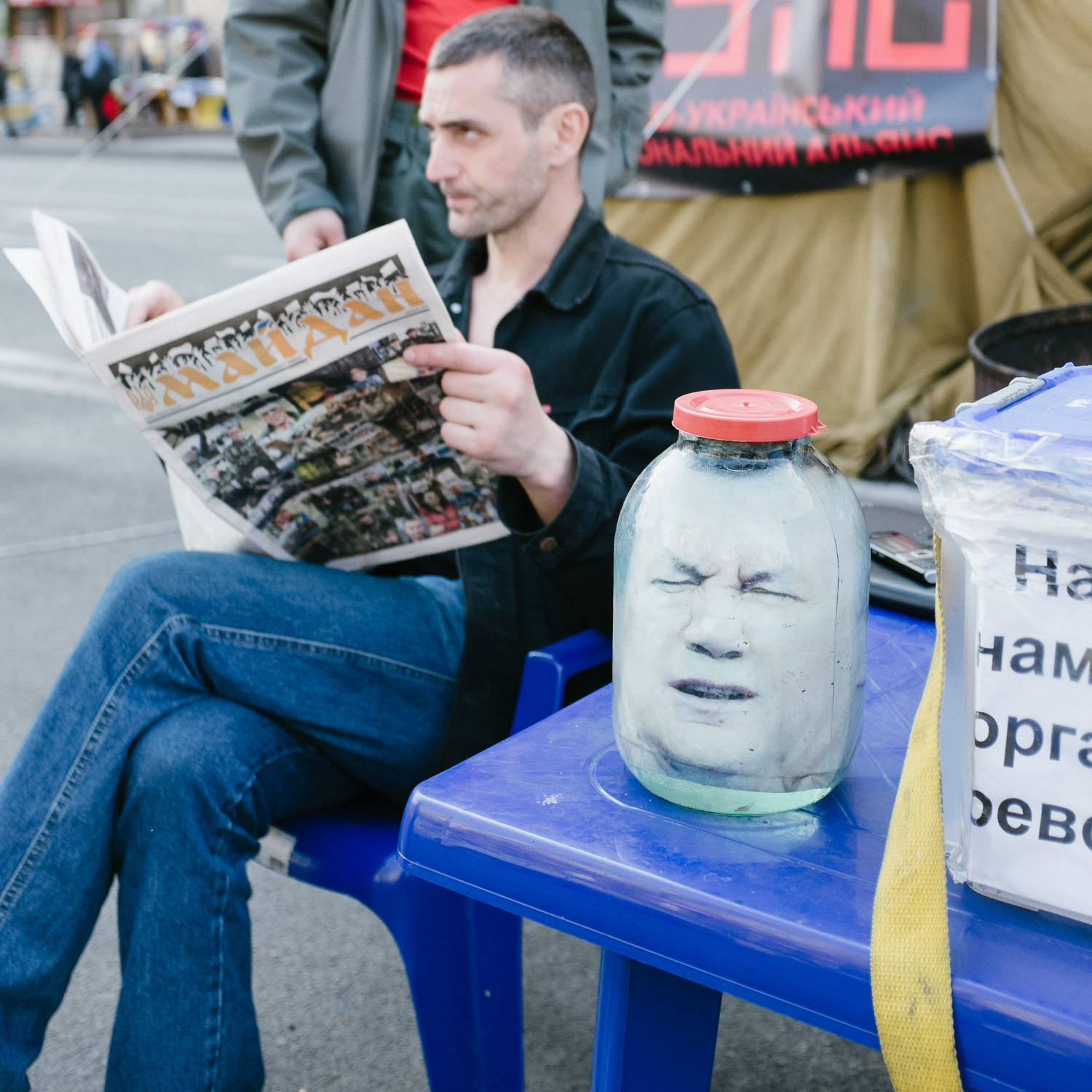  A man reads from a free newspaper reporting on the Euromaidan uprisings next to a replica head of former president Viktor Yanukovych in a sealed jar. 