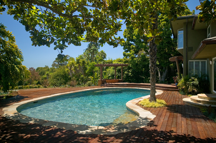 Kidney shaped pool with wood deck, pool stone coping, stairs and bench; blending natural colors of wood and stone.