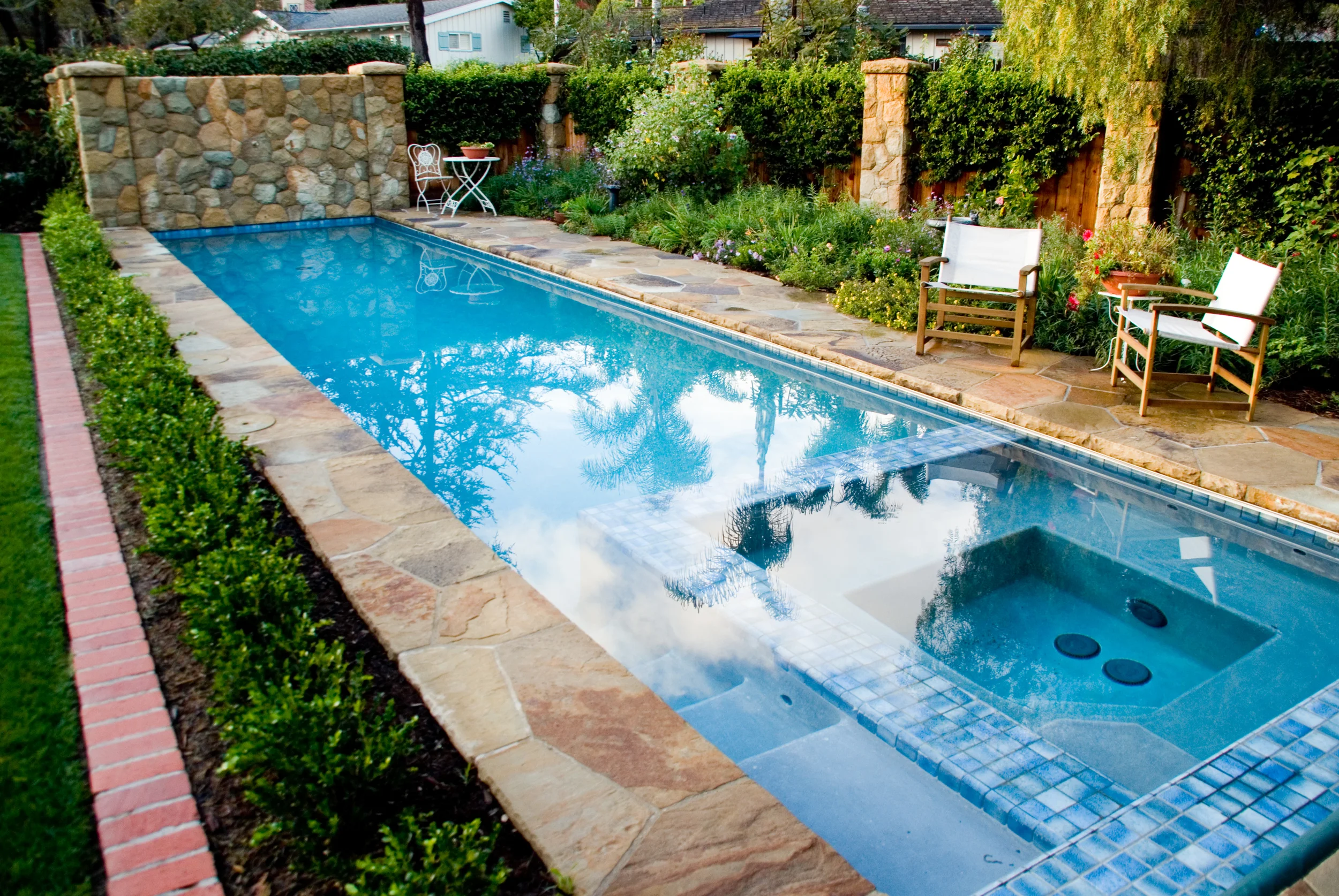 Long swimming pool with inset spa, long gradual steps lead into pool snugly fit between spa and pool side. Decorative variegated blue tile surround spa, blending into the shimmering pool waters.