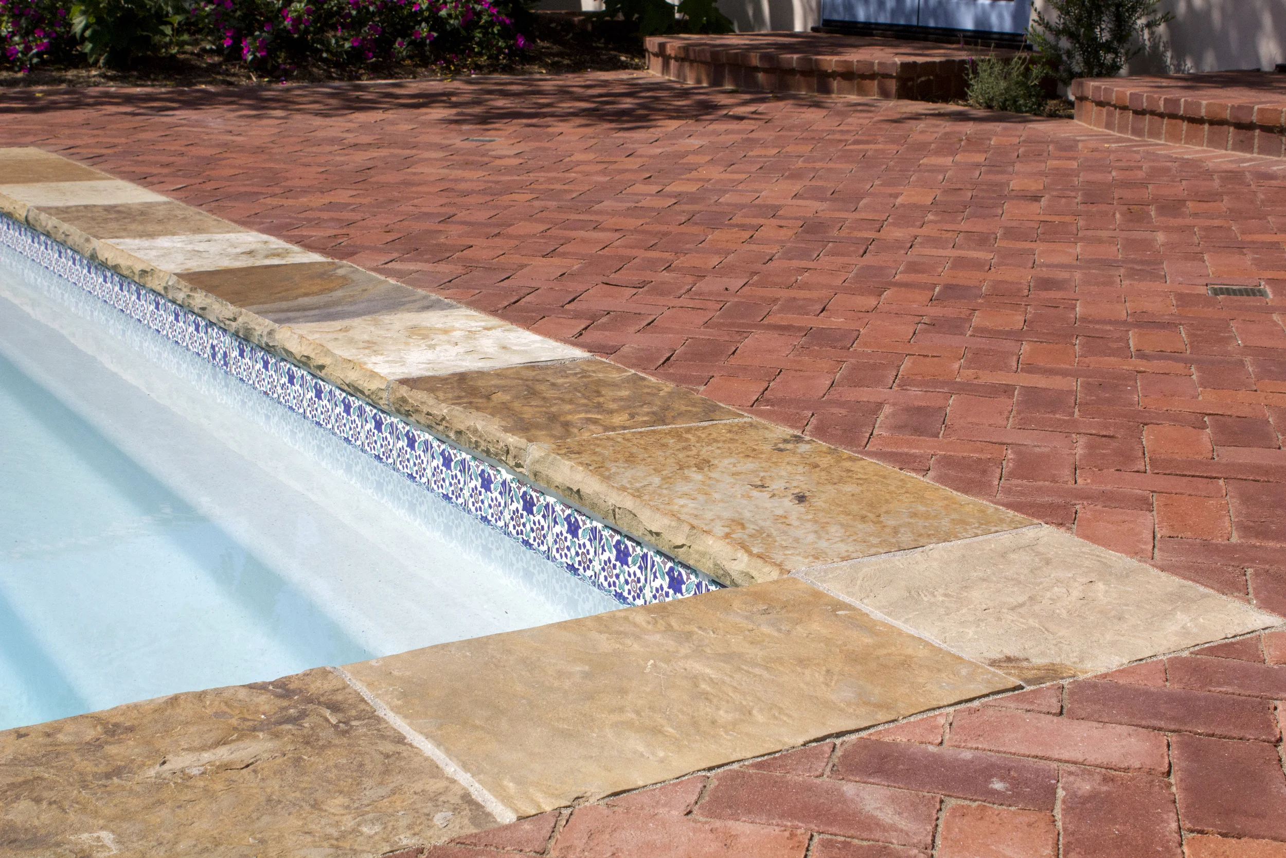 A mixture of stone materials (brick and flagstone) leading to pool’s edge with set in decorative tile along the water line highlighting classic white plaster pool finish.