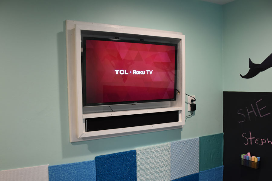 Recessed TV covered with plexiglass. Combination of smart TV and soundbar will give Landyn a calming environment when whale songs are streamed through the room