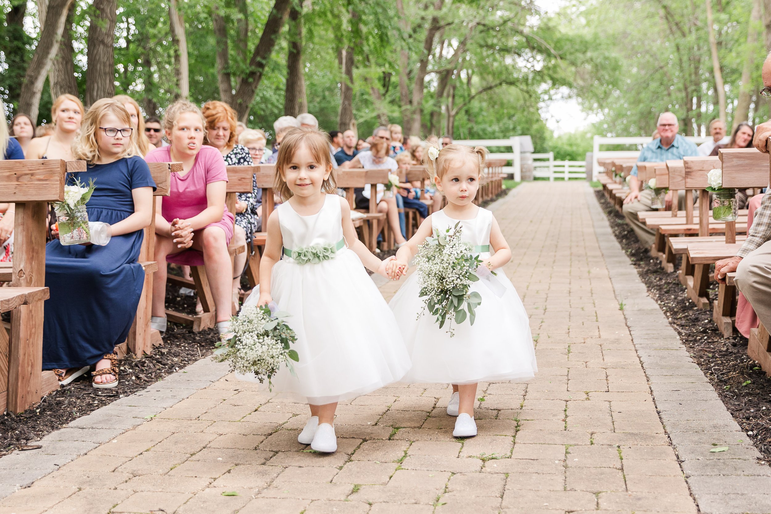 Flower girls walking down a paved aisle in an outdoor ceremony in Minnesota.