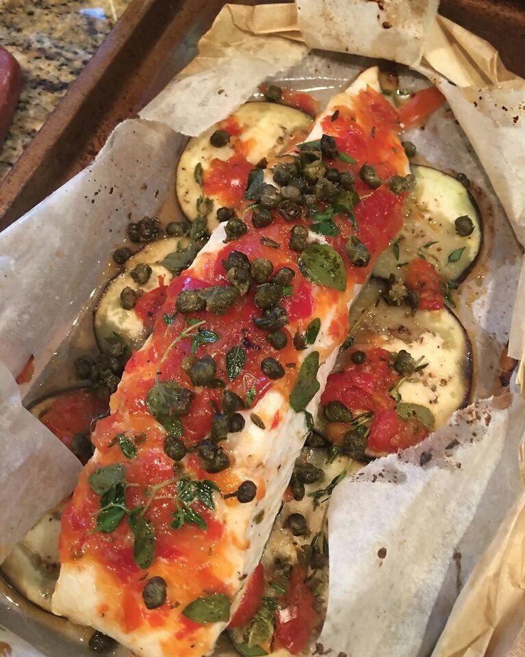 Parchment wrapped halibut on top of eggplant, topped with spicy red pepper relish, garden herbs and fried capers