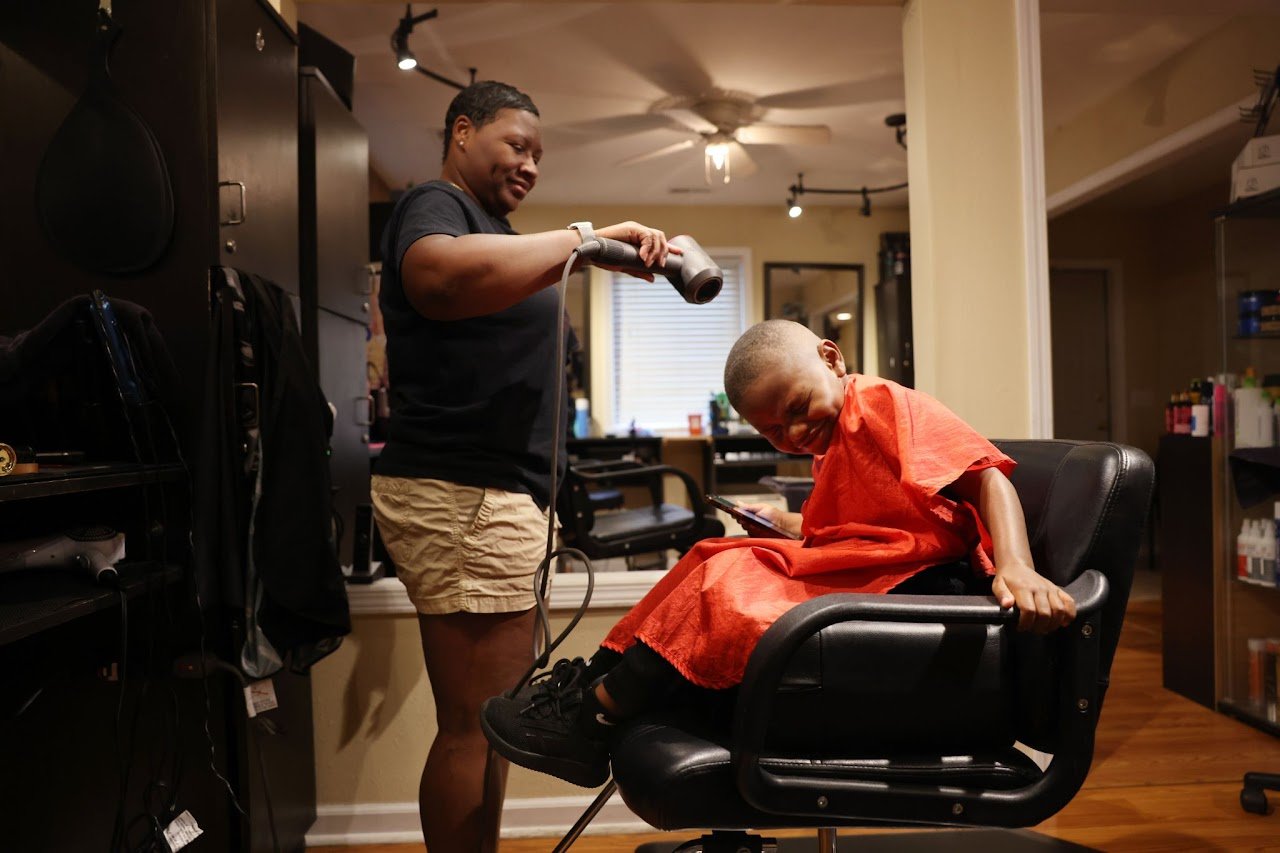  Carter laughs while his grandmother, Oola Staten, 45, blows hair clippings off of his neck after a haircut at her salon, Oola’s Beauty Shop. Due to his mother’s drug use and other legal issues, Oola has been Carter’s legal guardian since 2019. 