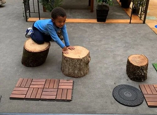 Children have been using the wood stumps to balance while going from one stump to the other. They try balancing while standing or crawling, as seen in the picture. Children also use the stumps to sit on and take a break or have conversations such as during dramatic play. Children have been exploring the stump sides and feeling different textures and edges.