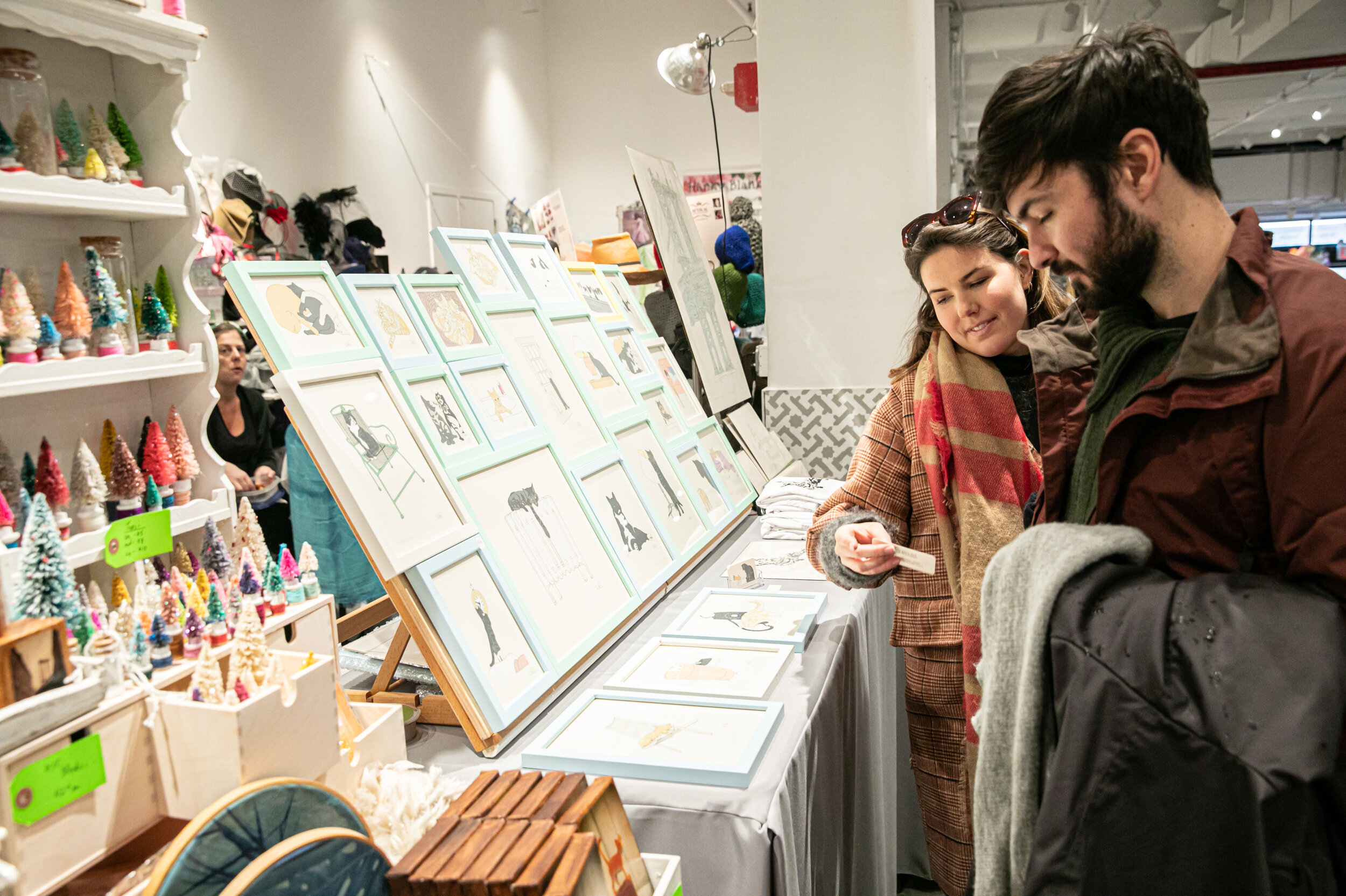 A couple are looking at a display of prints at a craft fair