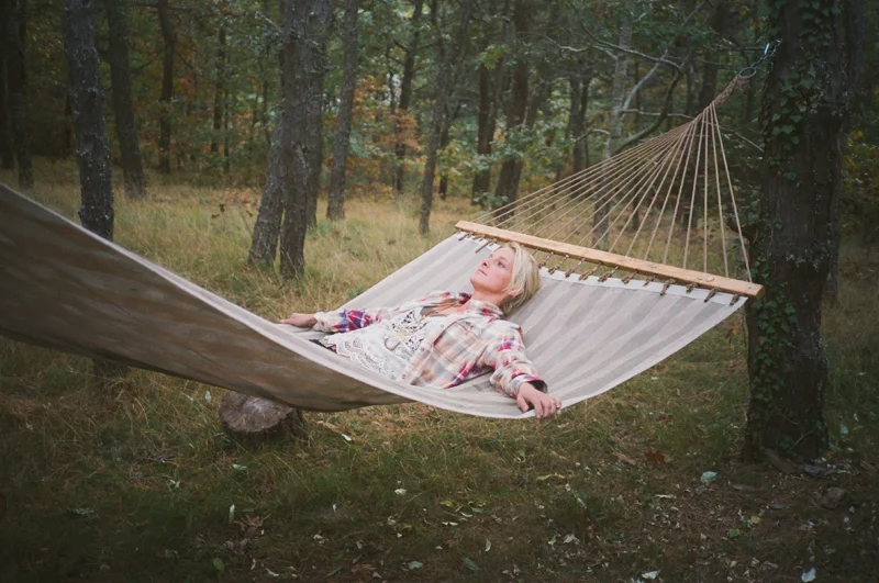 Woman relaxing on a hammock tied between trees in a wooded area.