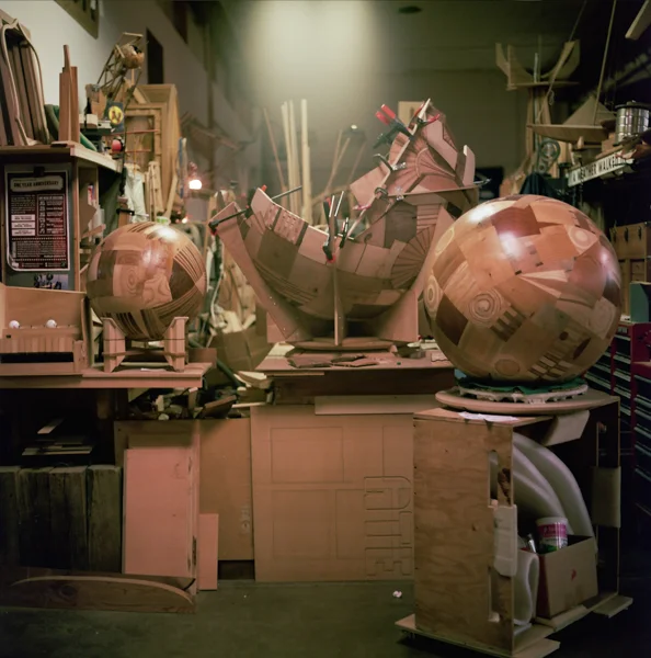 Workshop with various art supplies and large spherical sculptures, some wrapped in newspaper, on cluttered workbenches.