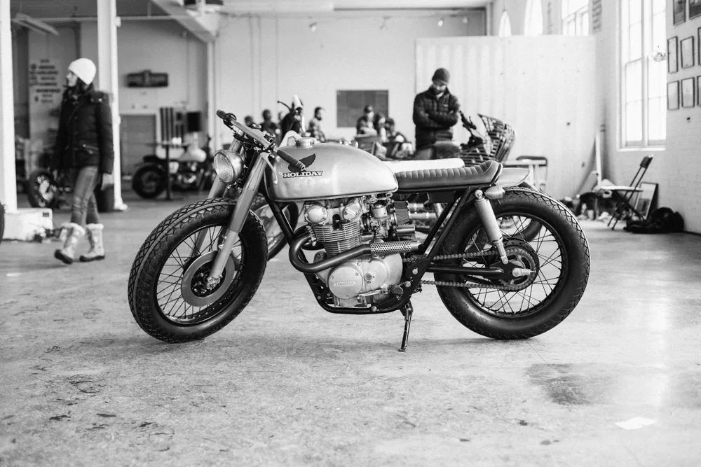 Black and white photo of a vintage Honda motorcycle on display indoors with people in the background.