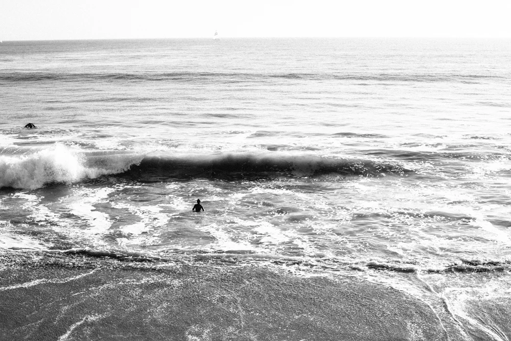 Two people swimming in the ocean near the beach with waves crashing