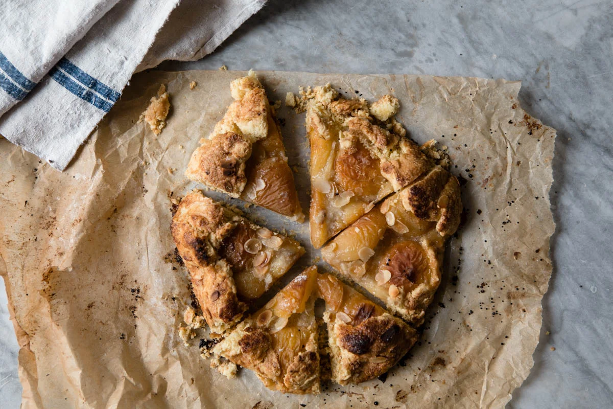 Freshly baked peach cobbler with sliced peaches and almond slices on top, sitting on parchment paper.