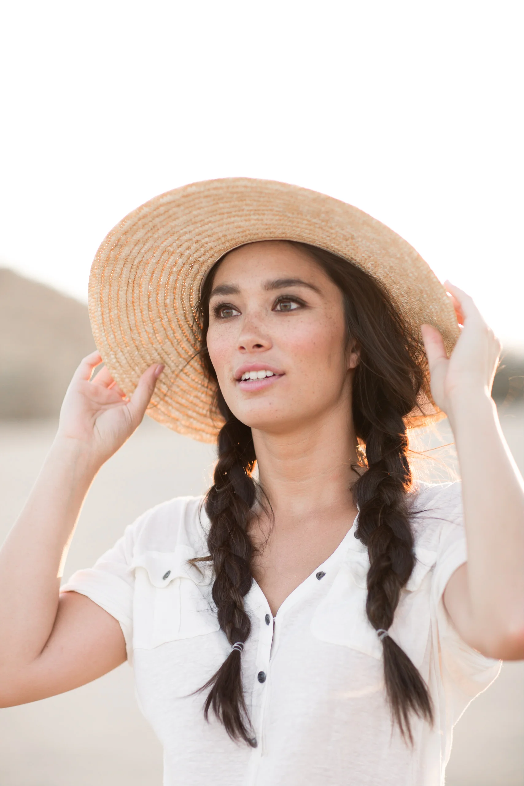 Young woman with dark braided hair wearing a large sun hat outdoors.