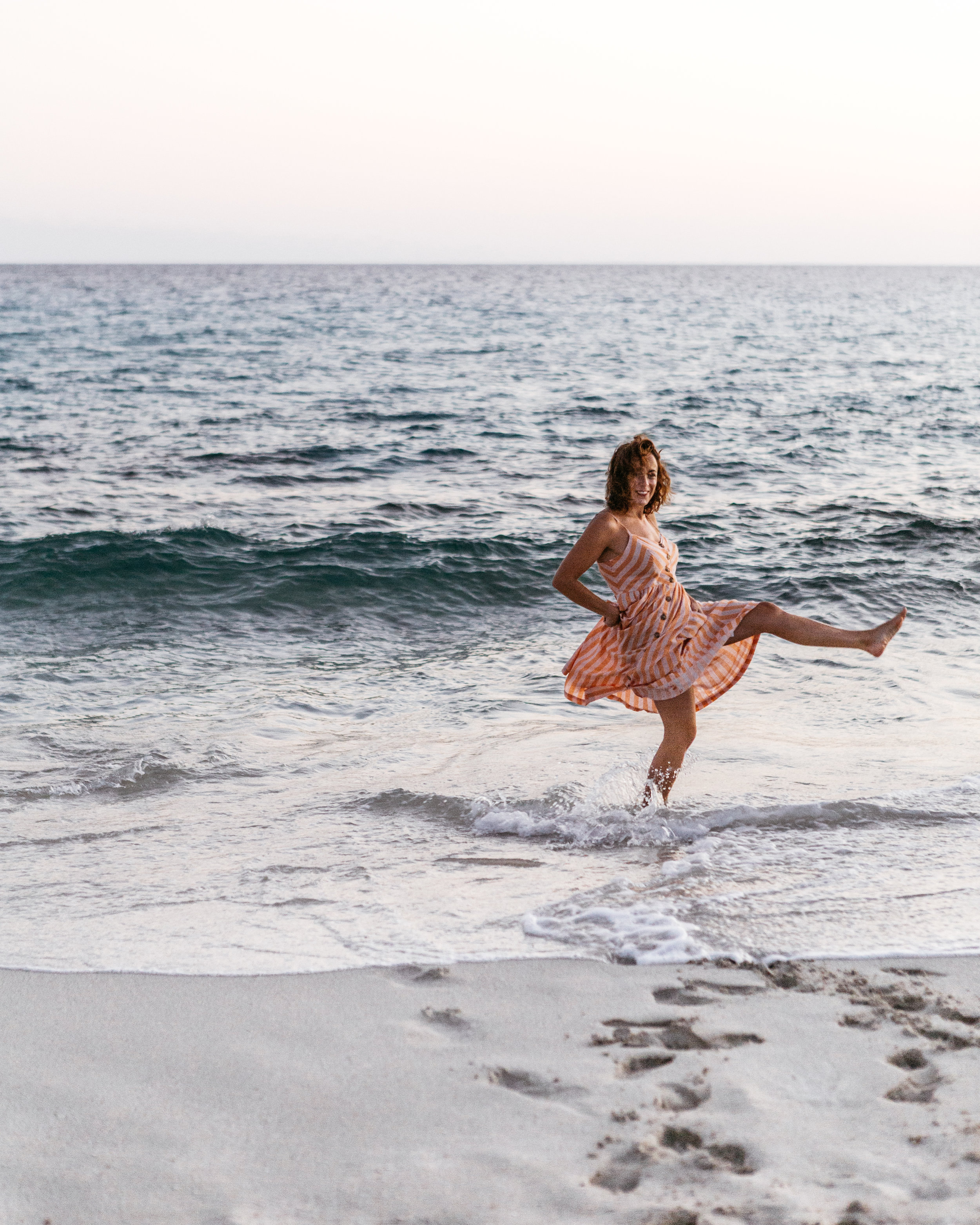 A woman in a striped dress playing in the ocean waves at sunset or sunrise.