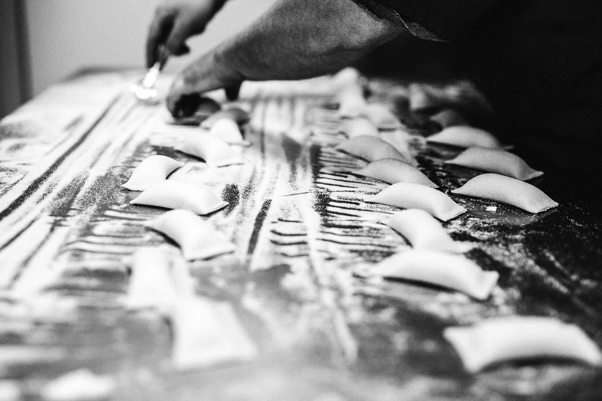 Close-up of a person's hand cutting or preparing pasta on a floured surface, with pieces of pasta arranged in rows.