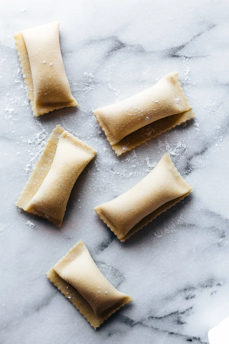Uncooked ravioli pasta on a floured marble surface.