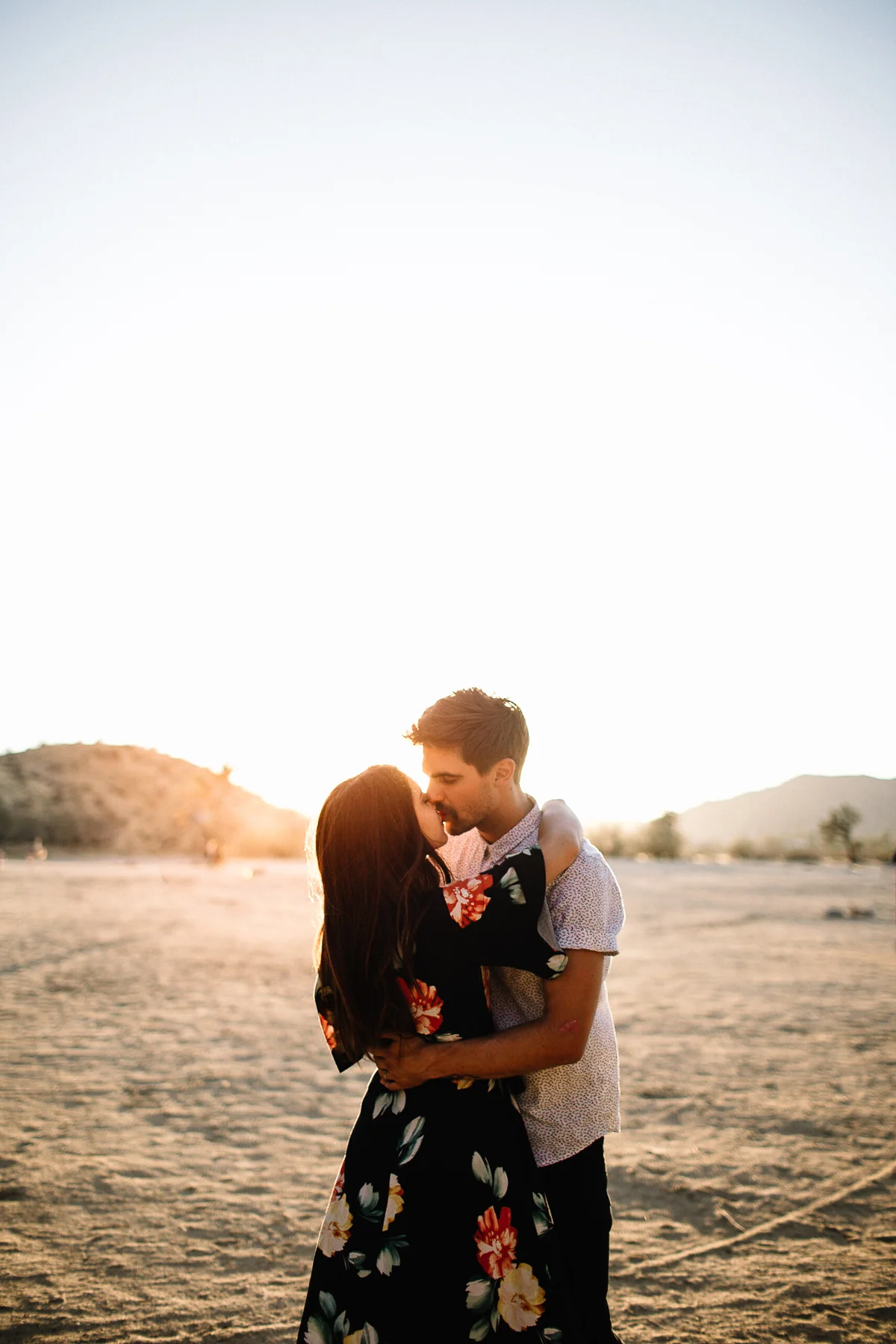 A couple embracing and kissing in a desert landscape during sunset.