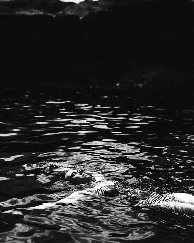 A person floating in dark water at night, with hills or mountains in the background.