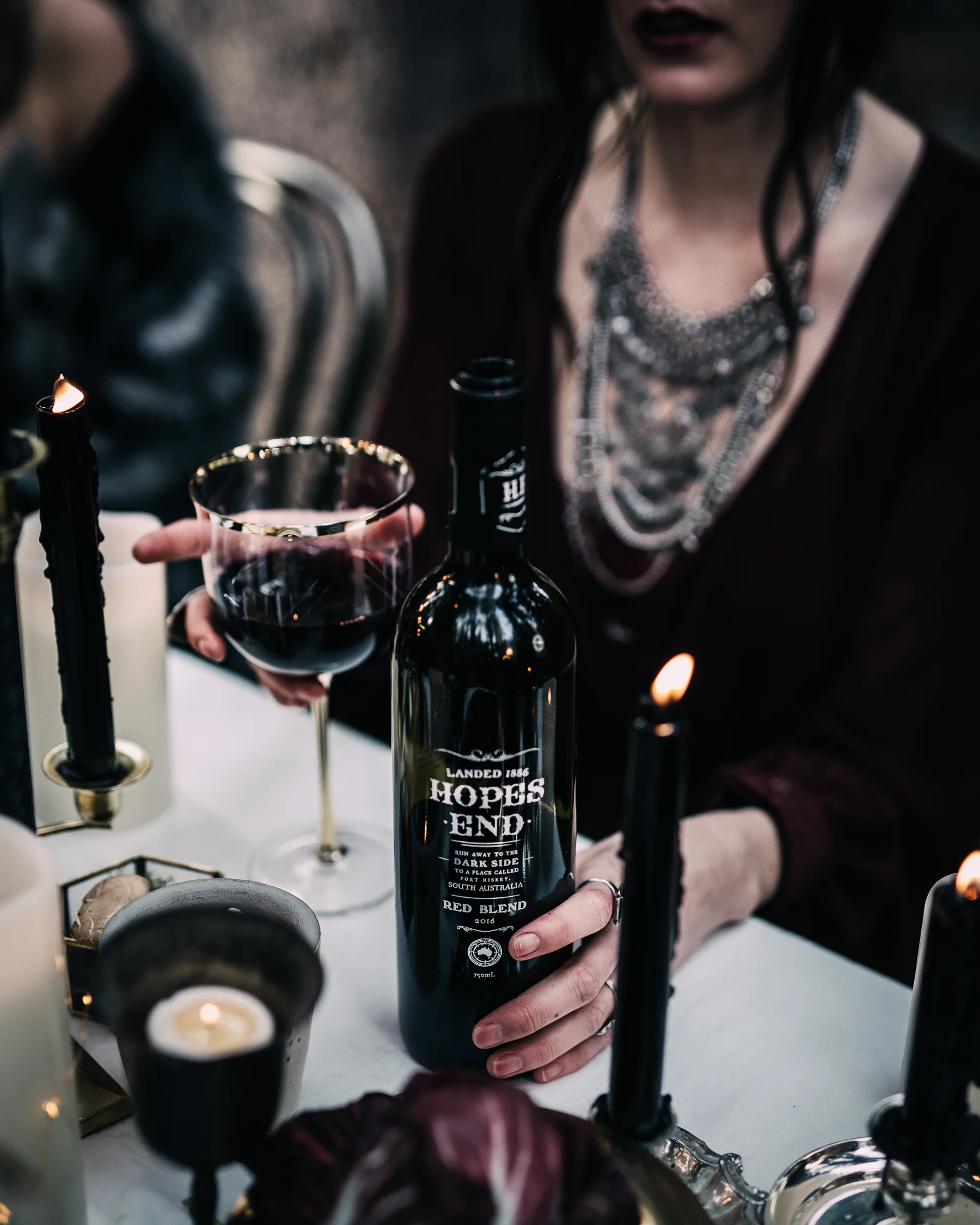 Person holding a wine bottle labeled "Hopes End" at a dinner table with candles and a wine glass.