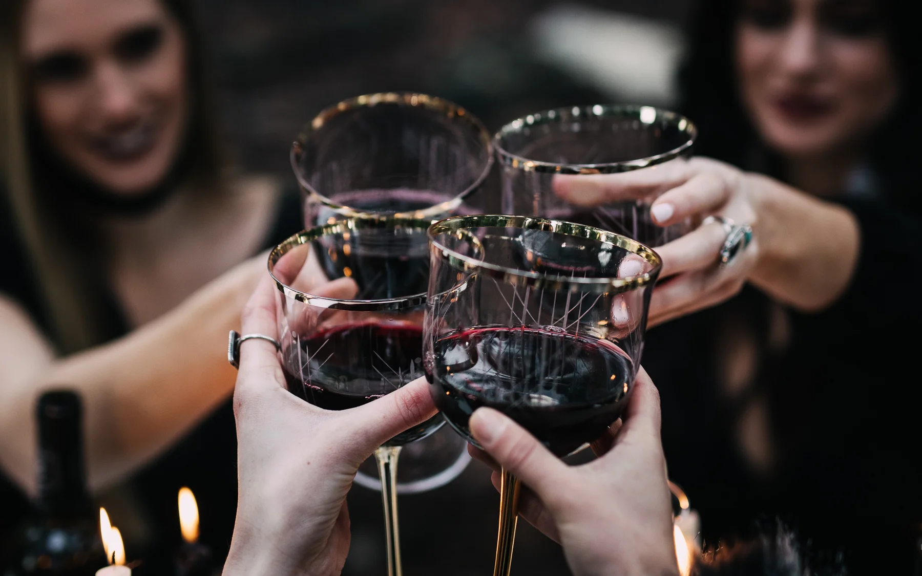 Four women clinking glasses of red wine during a toast at a celebration or gathering.
