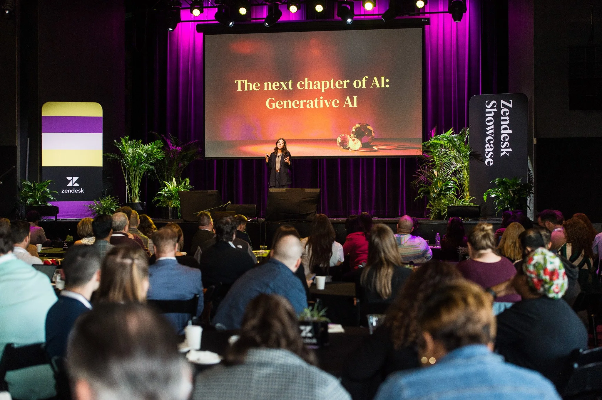 A speaker presenting on stage at a conference, with a slide titled 'The next chapter of AI: Generative AI', in front of an audience in a dark auditorium