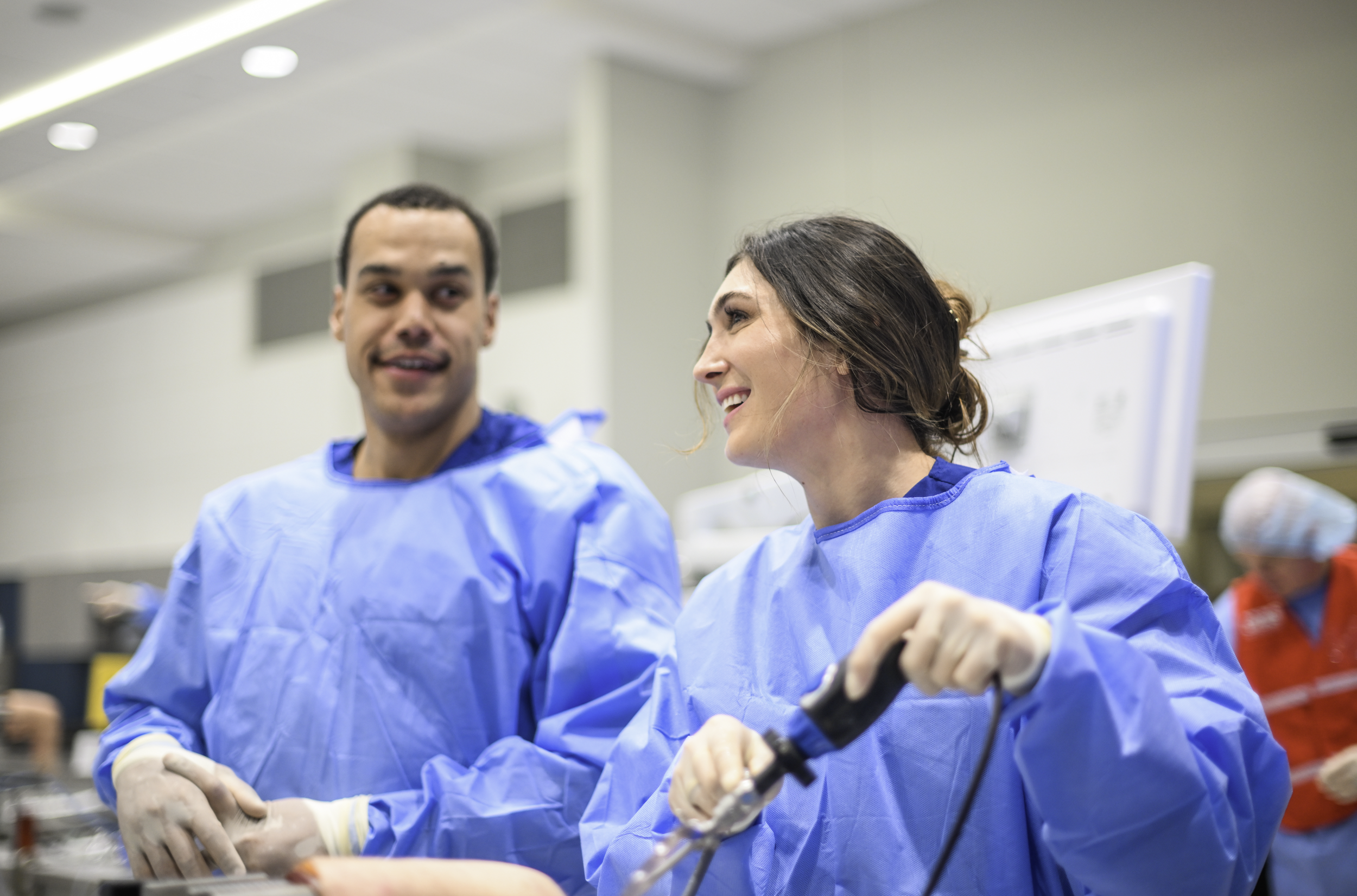 Two medical professionals in blue gowns smiling and talking during a medical procedure in a hospital setting.