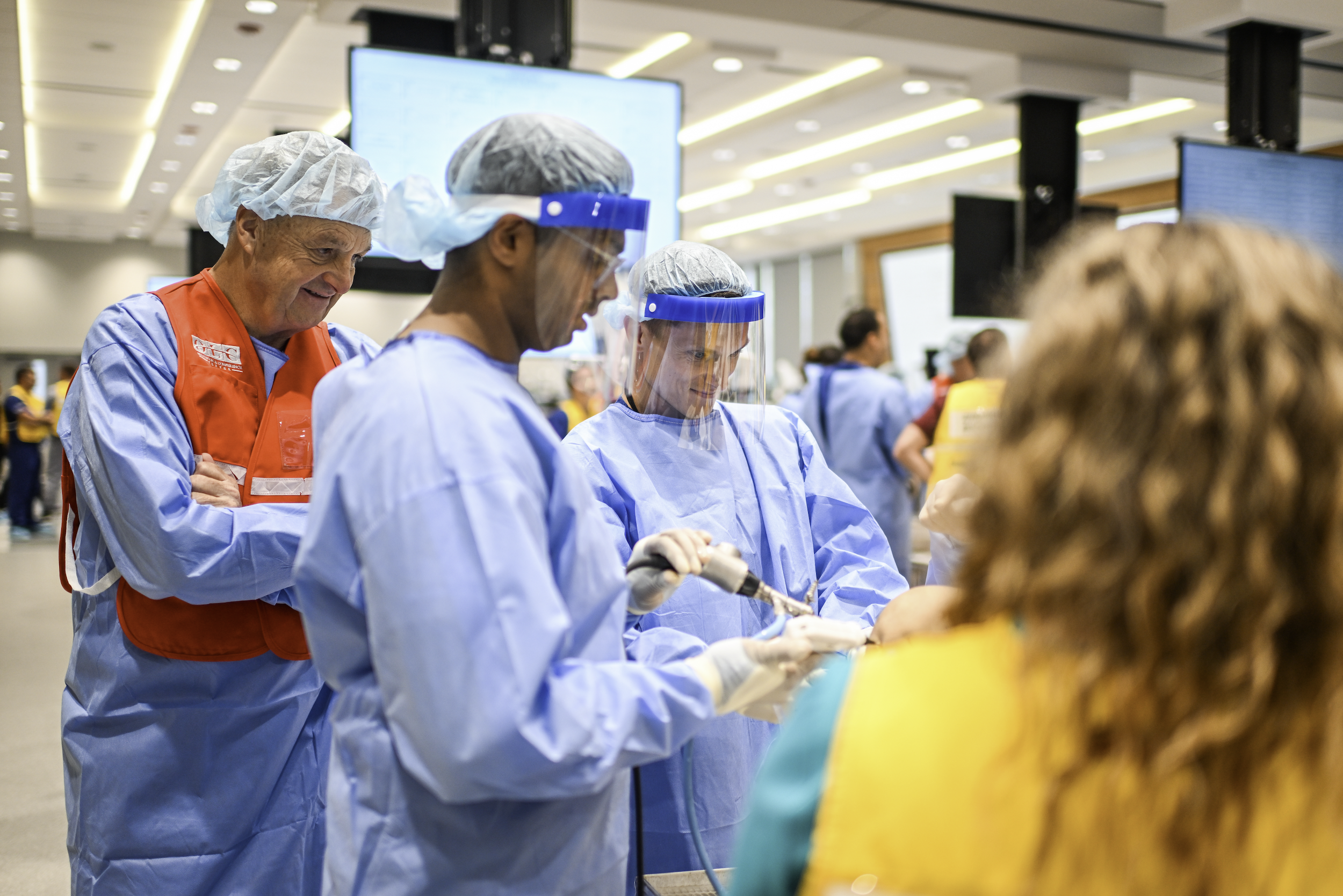 Healthcare workers in protective gear and scrubs preparing a medical procedure in a busy hospital setting.