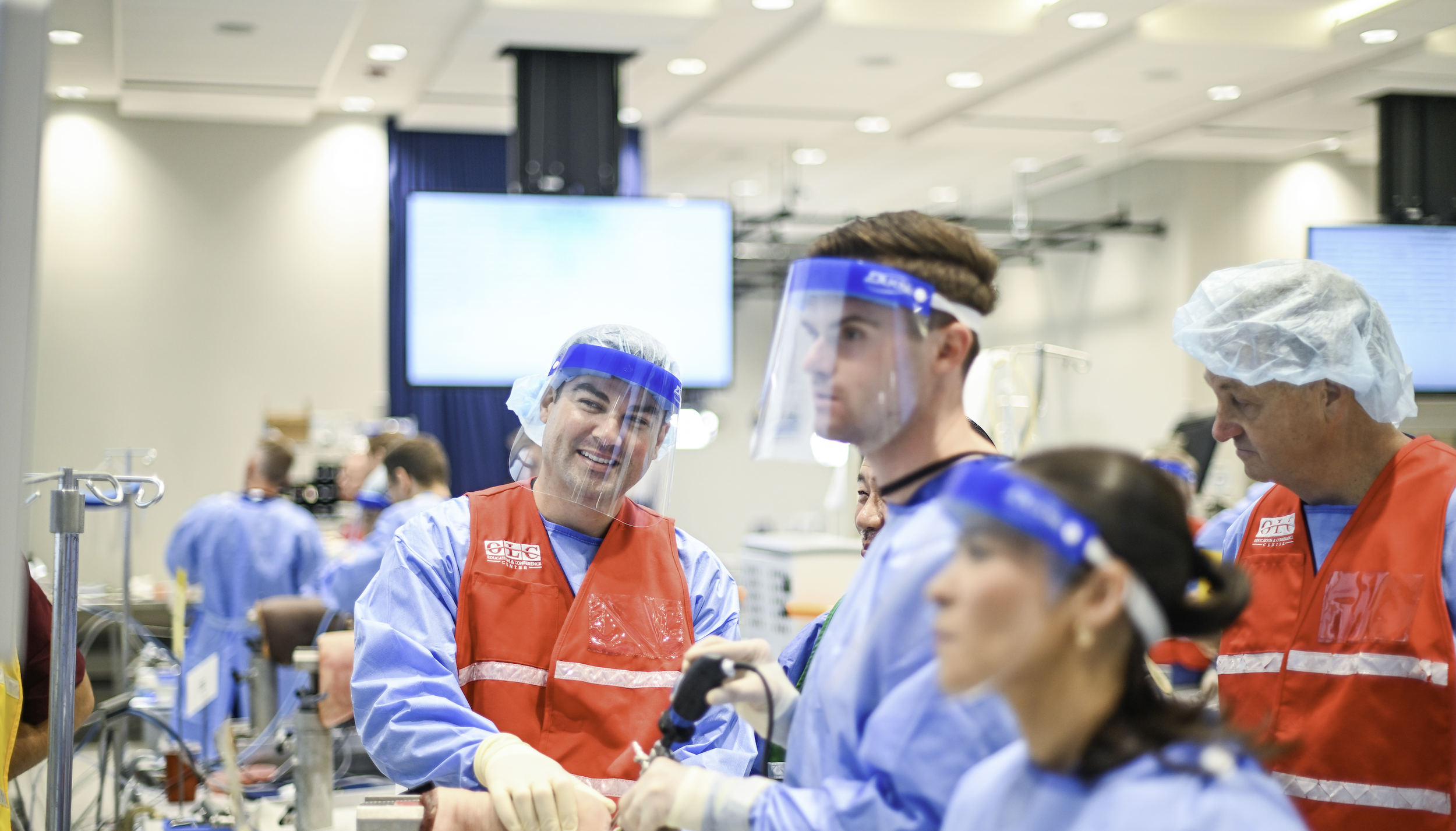 Medical professionals in scrubs, face shields, and hair coverings working together in a hospital setting.