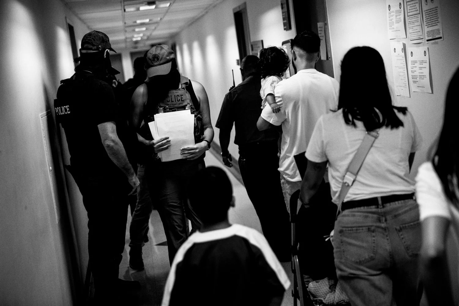  8:57AM: A family walks past federal agents towards a courtroom at the Jacob K Javits Federal Building in New York on 16 July 2025. Only the father had an immigration hearing, and he would later be detained by federal agents after leaving his hearing