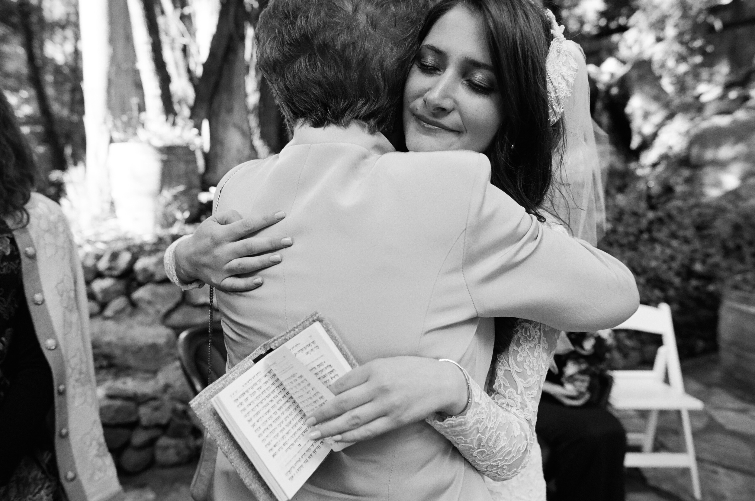 best destination wedding photographer photographs malibu wedding with orthodox jewish bride hugs grandmother while holding biblical text. 