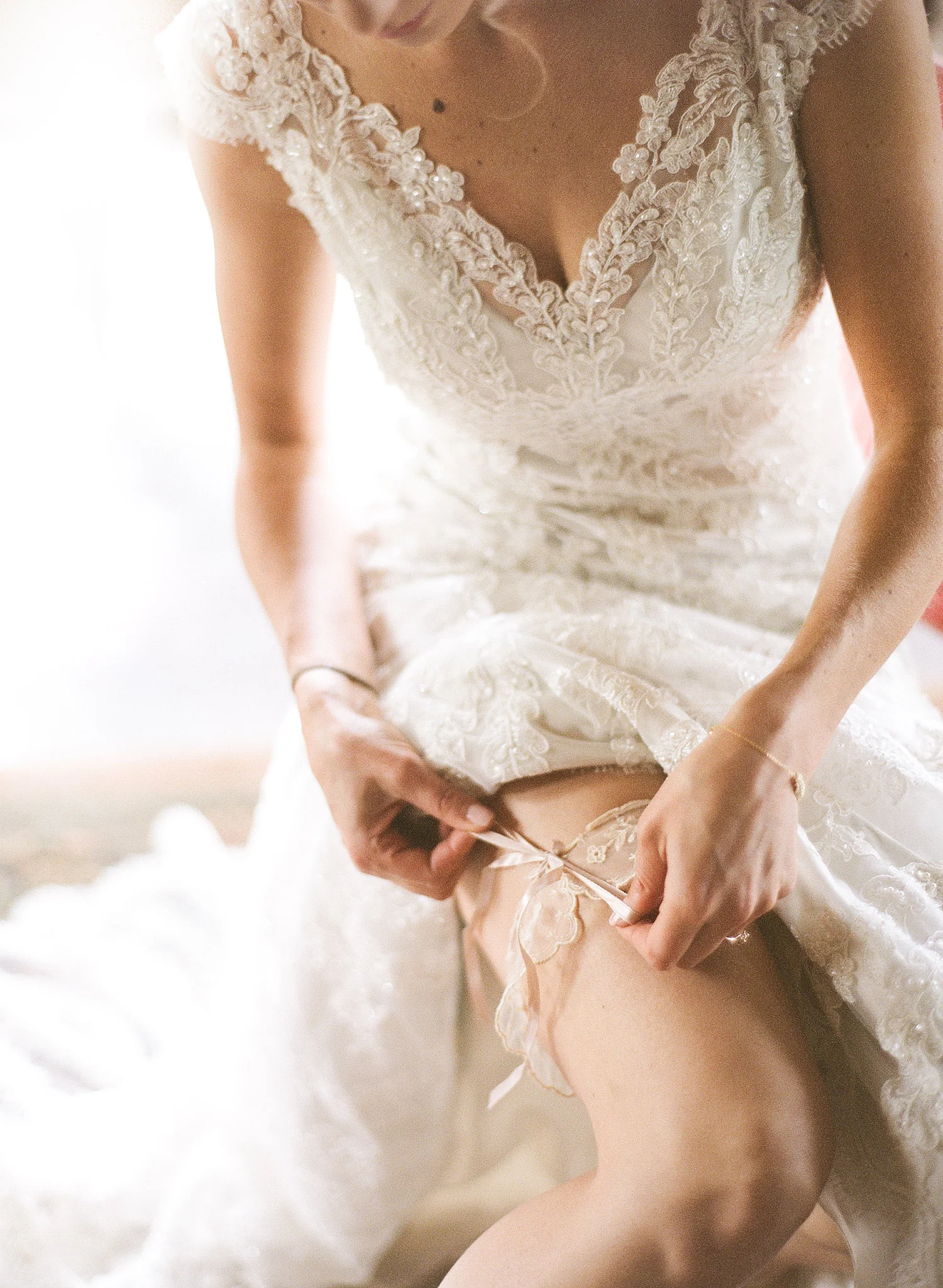 Bride ties on vintage lace garter on her wedding day while destination wedding photographer Lexia Frank photographs this wedding on film at the Northwind Perennial Gardens in Wisconsin